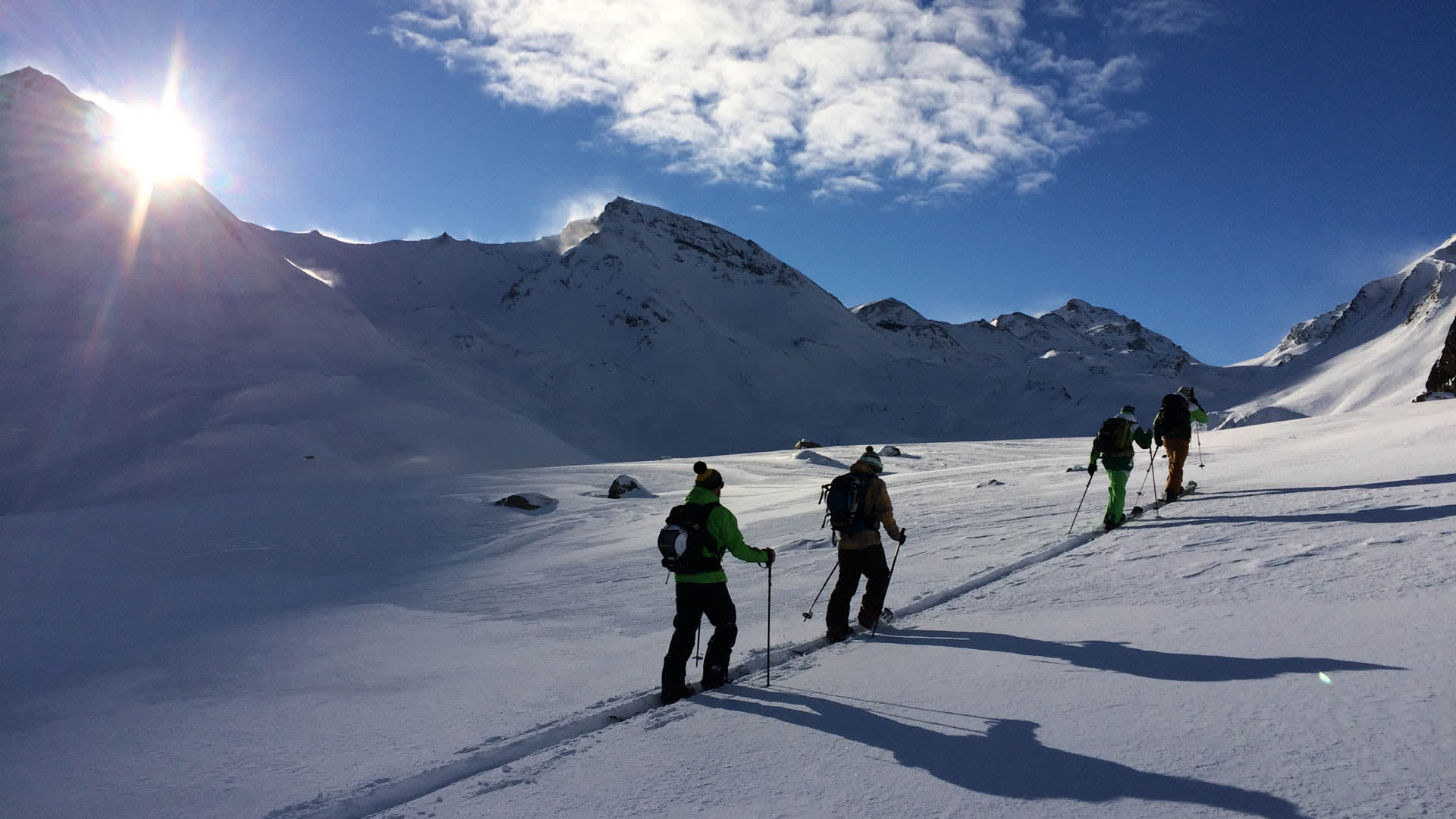 Vier Skitourengeher im Aufstieg auf verschneitem Hochplateau nahe der Heidelberger Hütte im Gegenlicht.