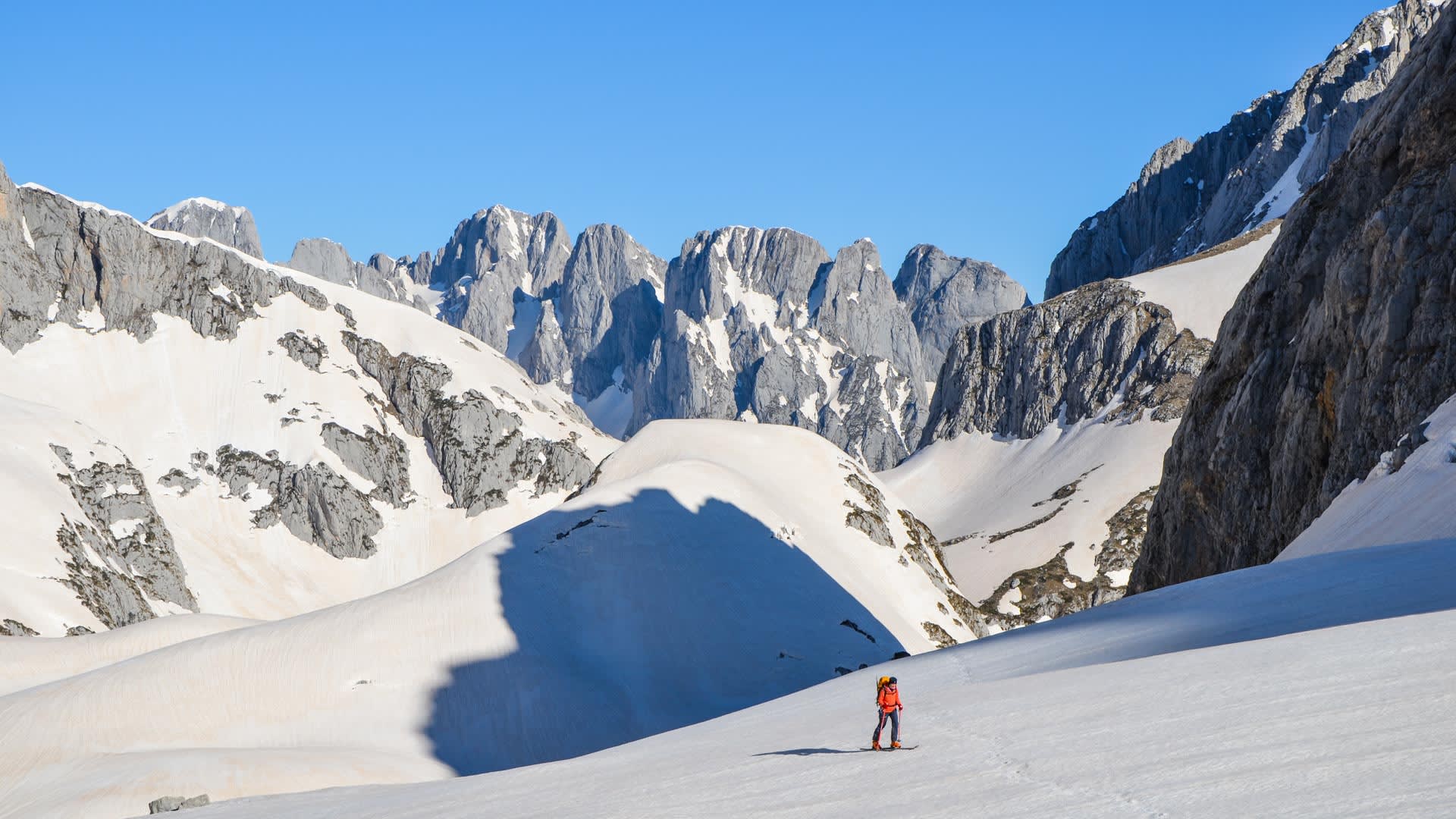 Ein Skitourengeher steigt einen weiten Schneehang im Durmitor-Nationalpark auf, im Hintergrund gezackte Kalksteinfelsen.