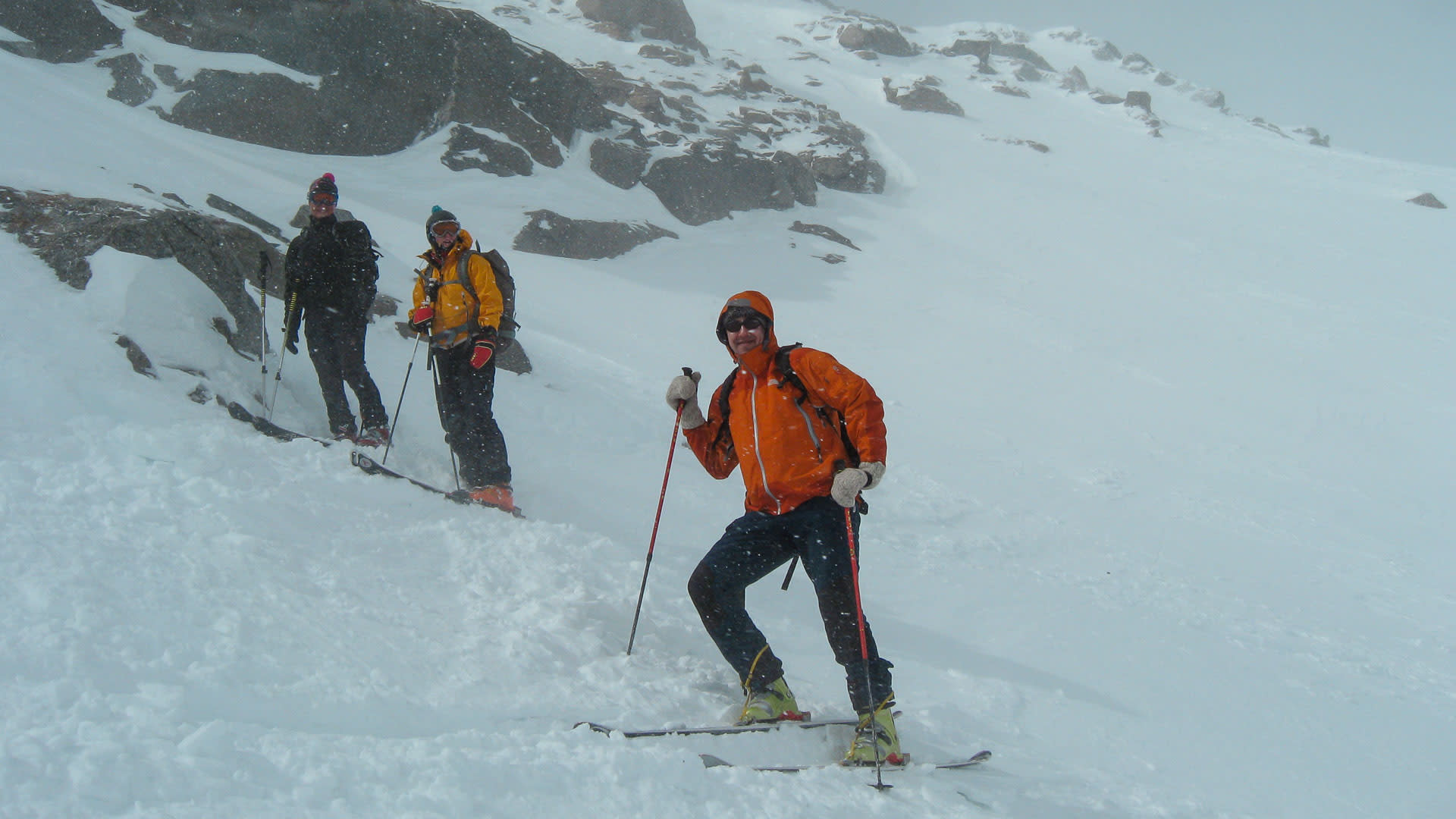 Drei Skitourengeher steigen mit Fellen bei Schneefall einen Berghang nahe der Sesvennahütte in Südtirol auf.