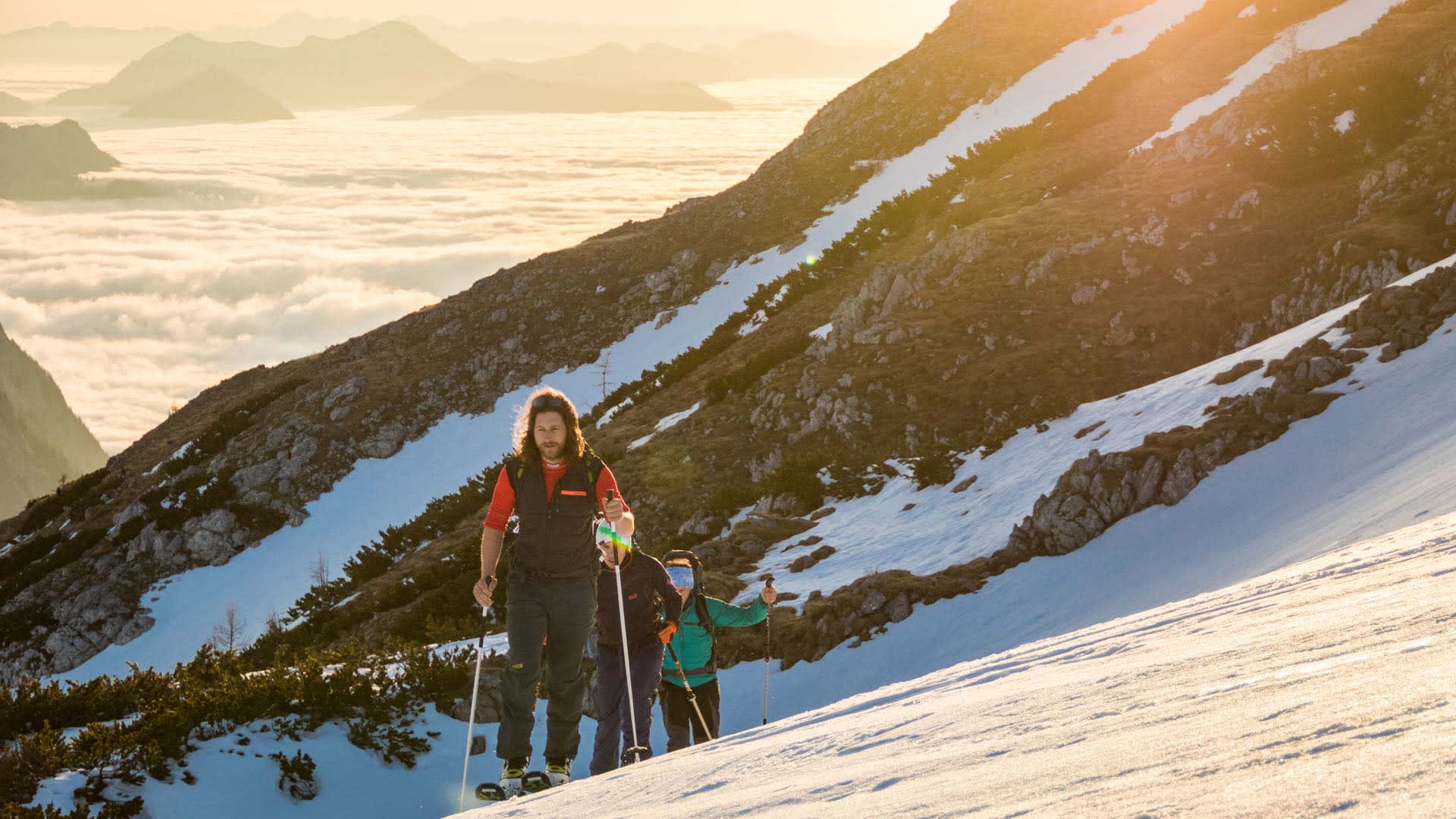 Drei Skitourengeher steigen mit Skistöcken einen verschneiten Hang zum Schneibstein auf.