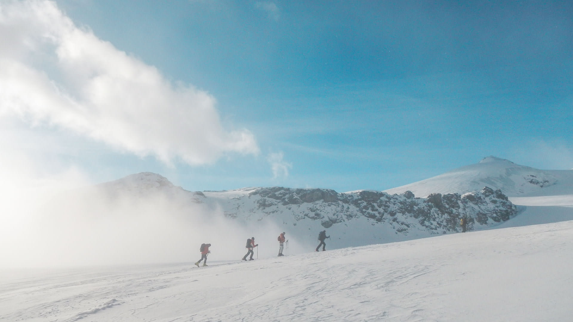 Fünf Skitourengeher steigen in einer Reihe über ein breites Schneefeld zum Strahlhorn im Wallis auf.