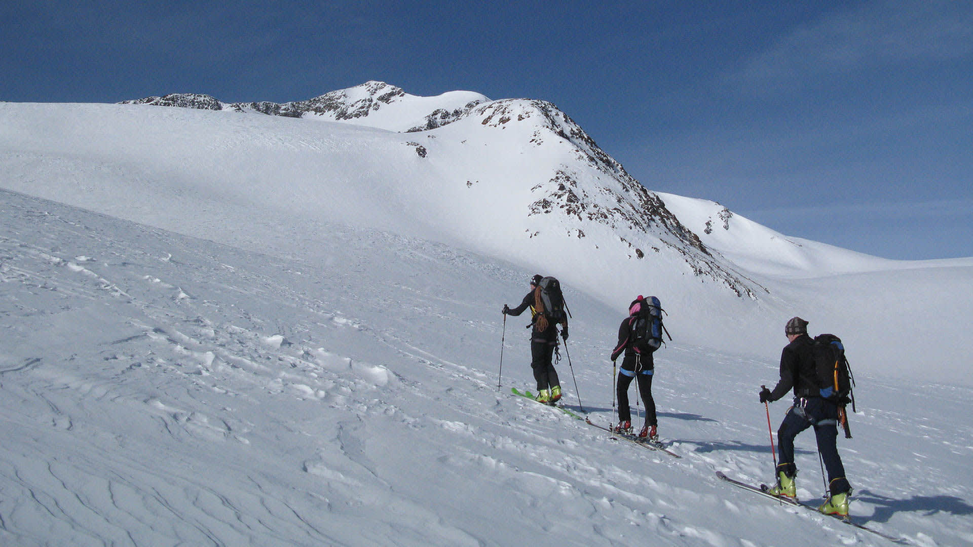 Drei Skitourengeher steigen mit Fellen und Rucksäcken einen breiten Schneehang in Südtirol auf.