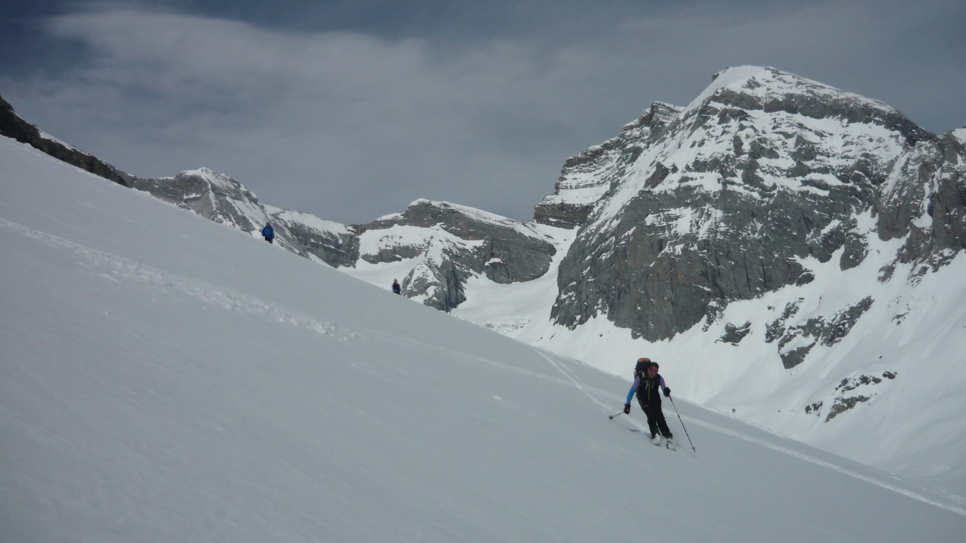 Drei Skitourengeher steigen einen steilen Schneehang zum Tödi auf, im Hintergrund eine markante Felswand.