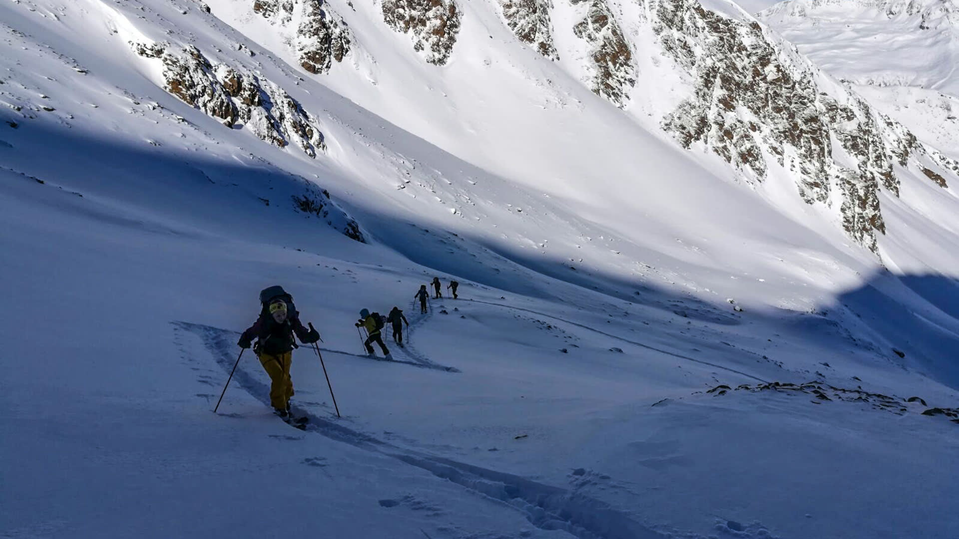 Sechs Skitourengeher steigen in Einzelreihe mit Fellen einen verschneiten Hang im Vinschgau auf.