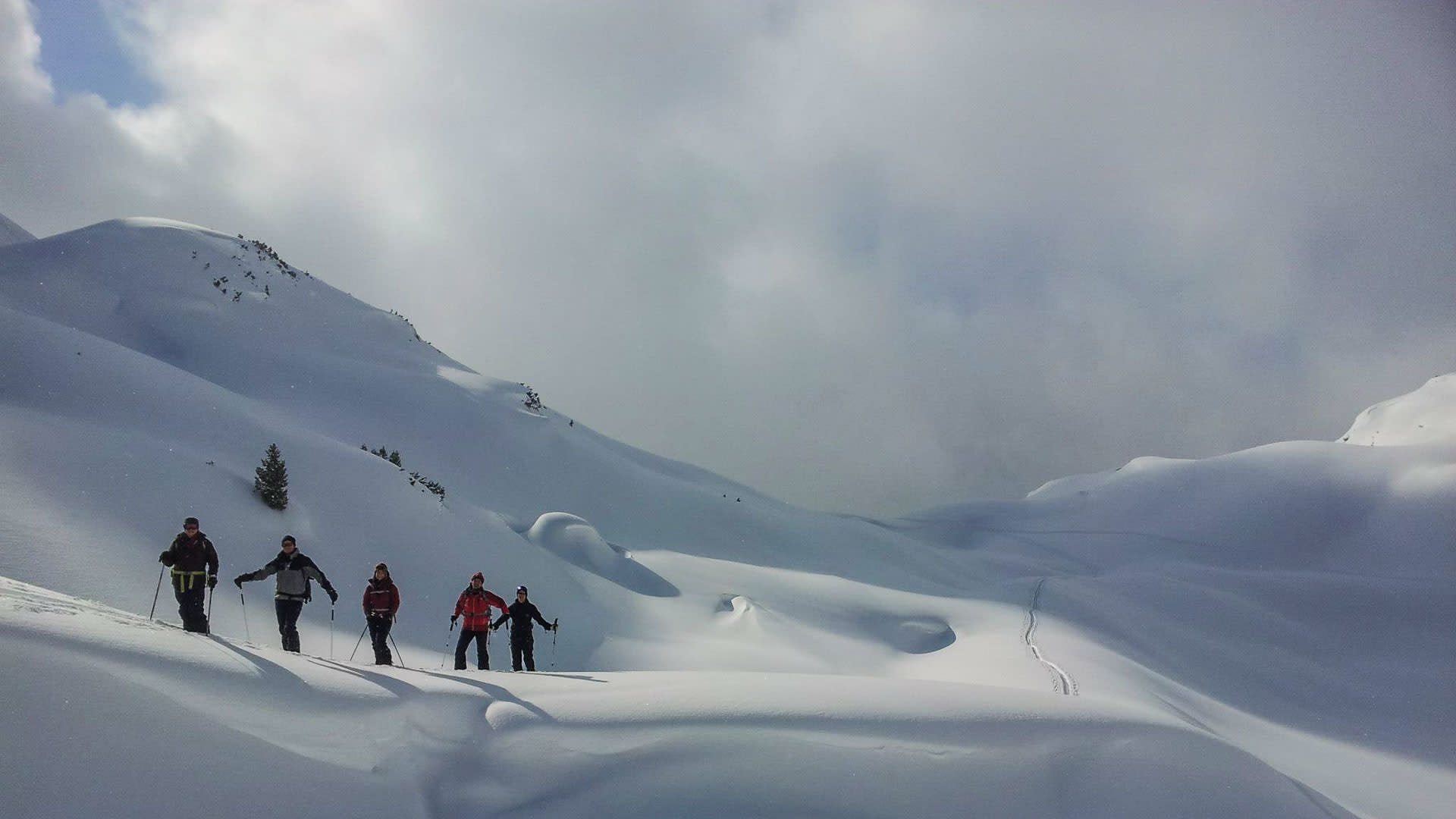 Fünf Skitourengeher mit Ski und Fellen auf einem verschneiten Hang in Österreich beim Aufstieg im Rofangebirge.