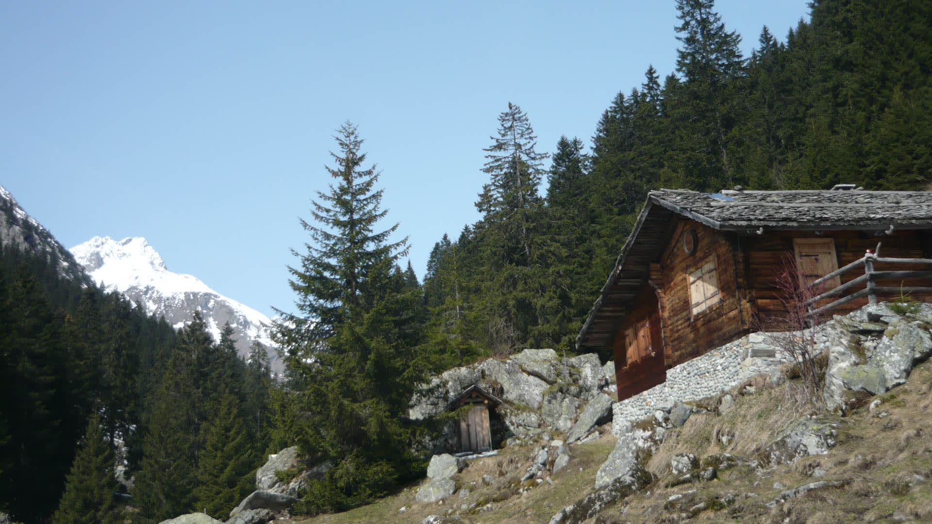 Traditionelle Holzhütte auf felsigem Hang als Stützpunkt für die Skitour zum Tödi, im Hintergrund schneebedeckter Gipfel