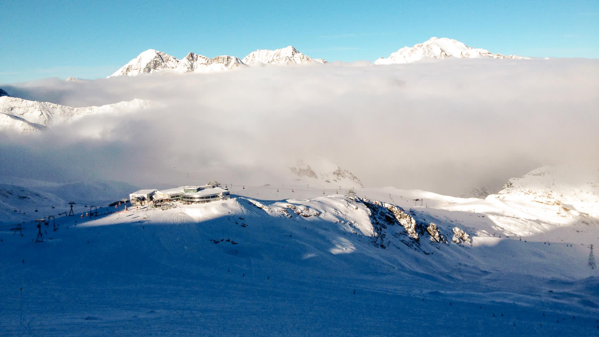 Stubaier Gletscher im Winter mit Bergstation, Skiliften und Wolkenmeer über dem Tal aus der Vogelperspektive.