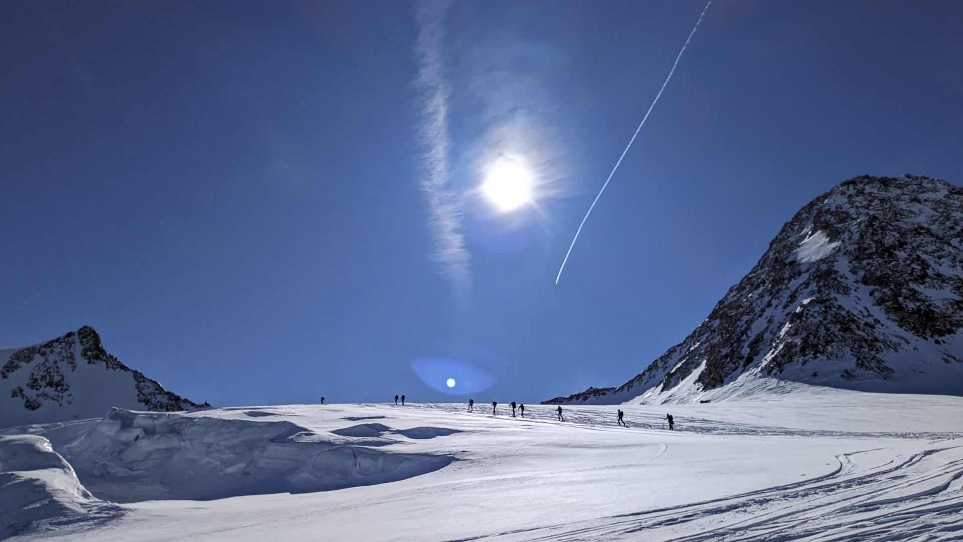 Gruppe von Skitourengehern traversiert das Gletscherplateau am Brochkogel unter wolkenlosem blauem Himmel.