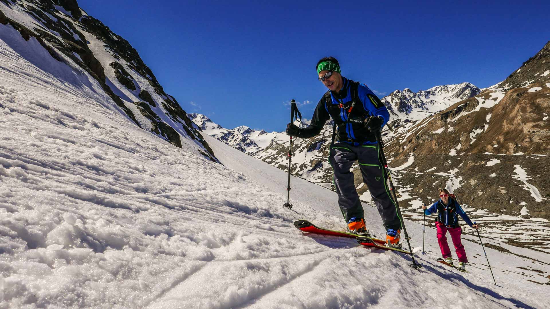 Zwei Skitourengeher steigen einen steilen Firnhang am Cevedale in Südtirol auf, blauer Himmel im Hintergrund.