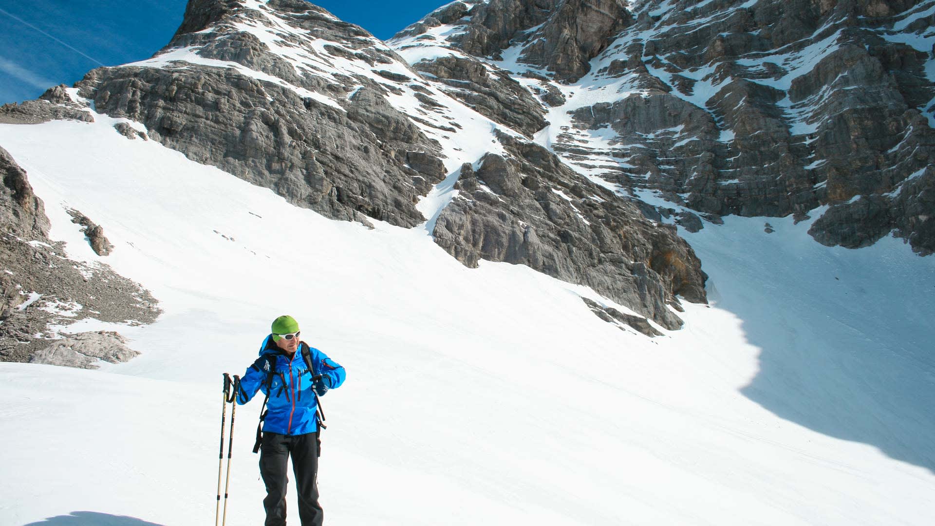 Freerider mit Trekkingstöcken am verschneiten Hang der Neuen Welt vor steiler Kalkstein-Felswand im Winter.