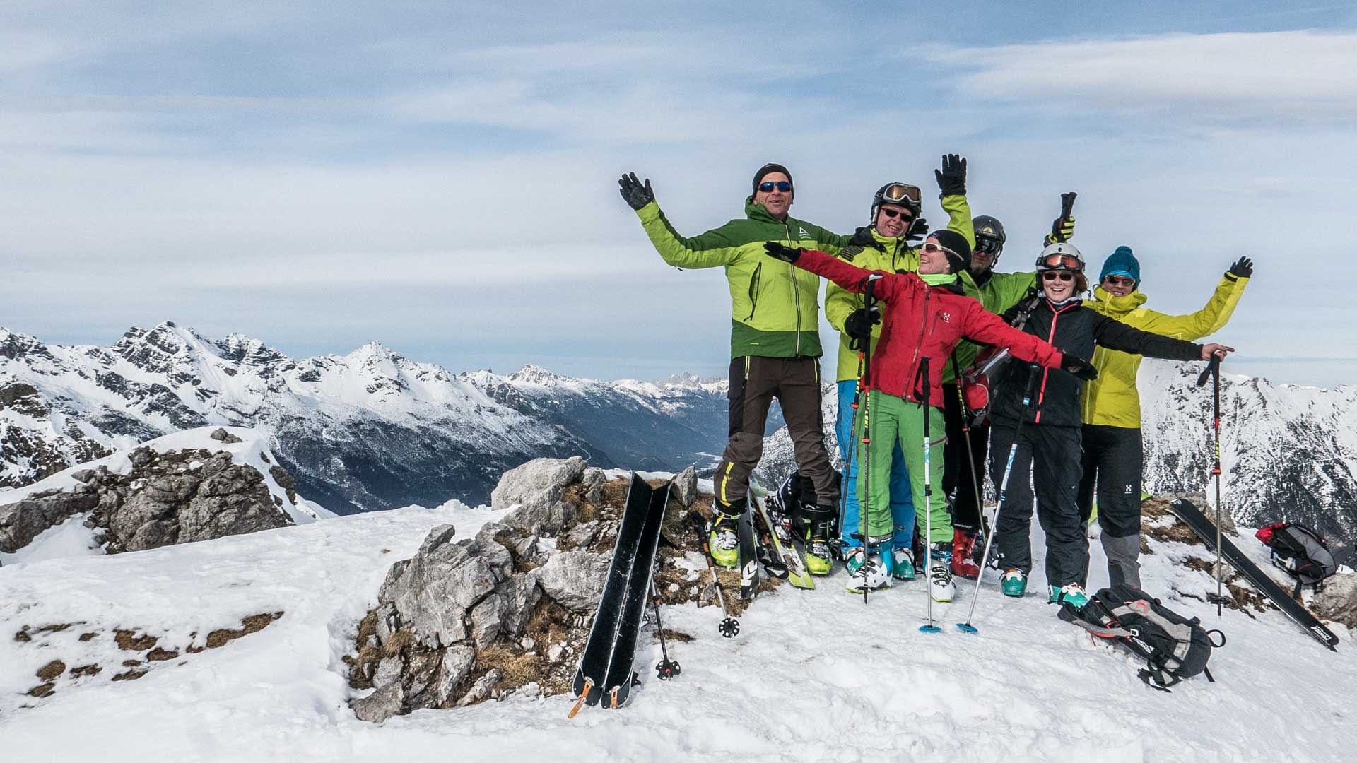 Sechs Skitourengeher stehen auf dem Schafkar-Gipfel in den Lechtaler Alpen und winken in die Kamera.