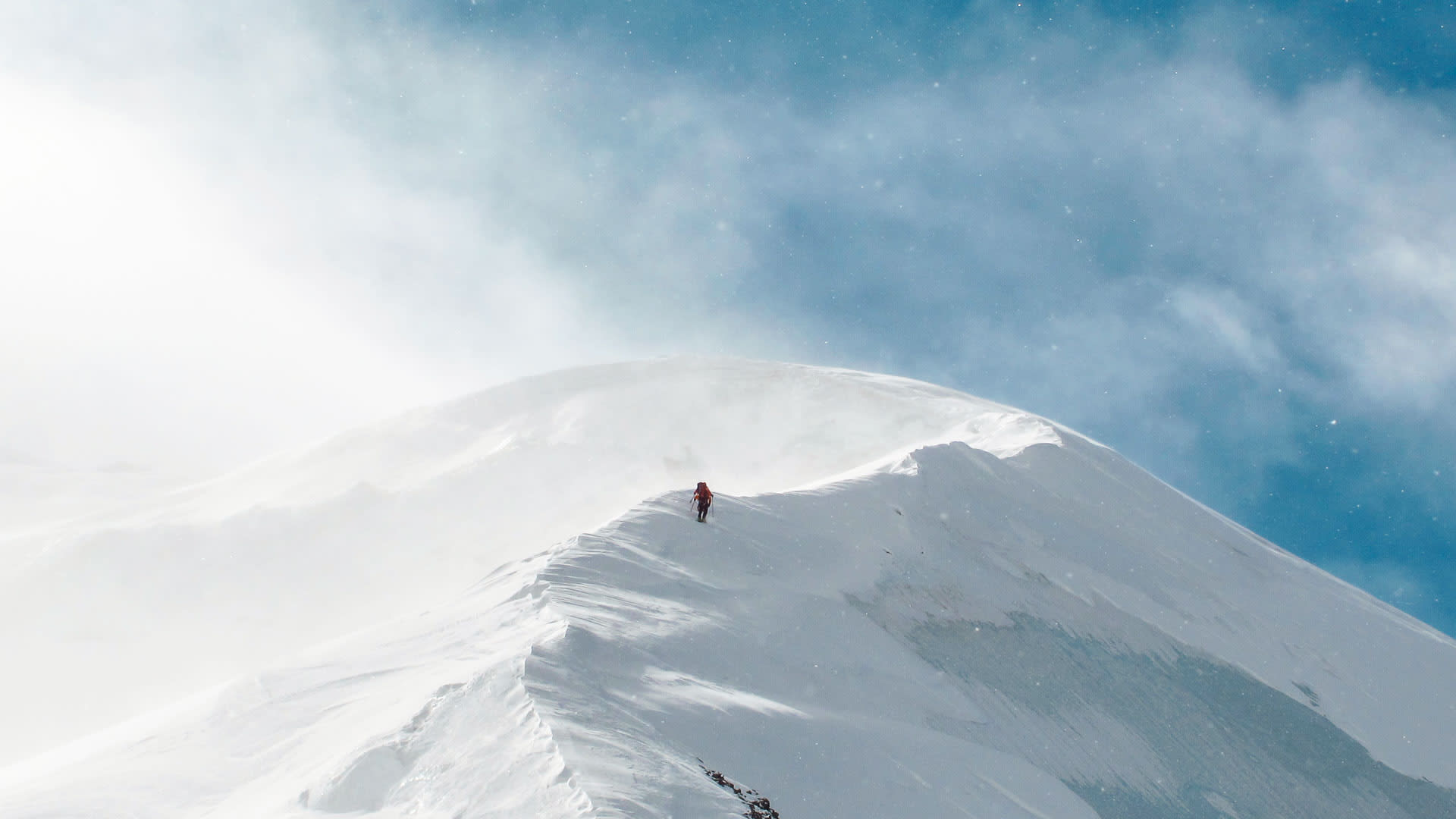 Skitourengeher steigt auf windgepeitschtem Schneegrat kurz unterhalb des Strahlhorn-Gipfels auf.