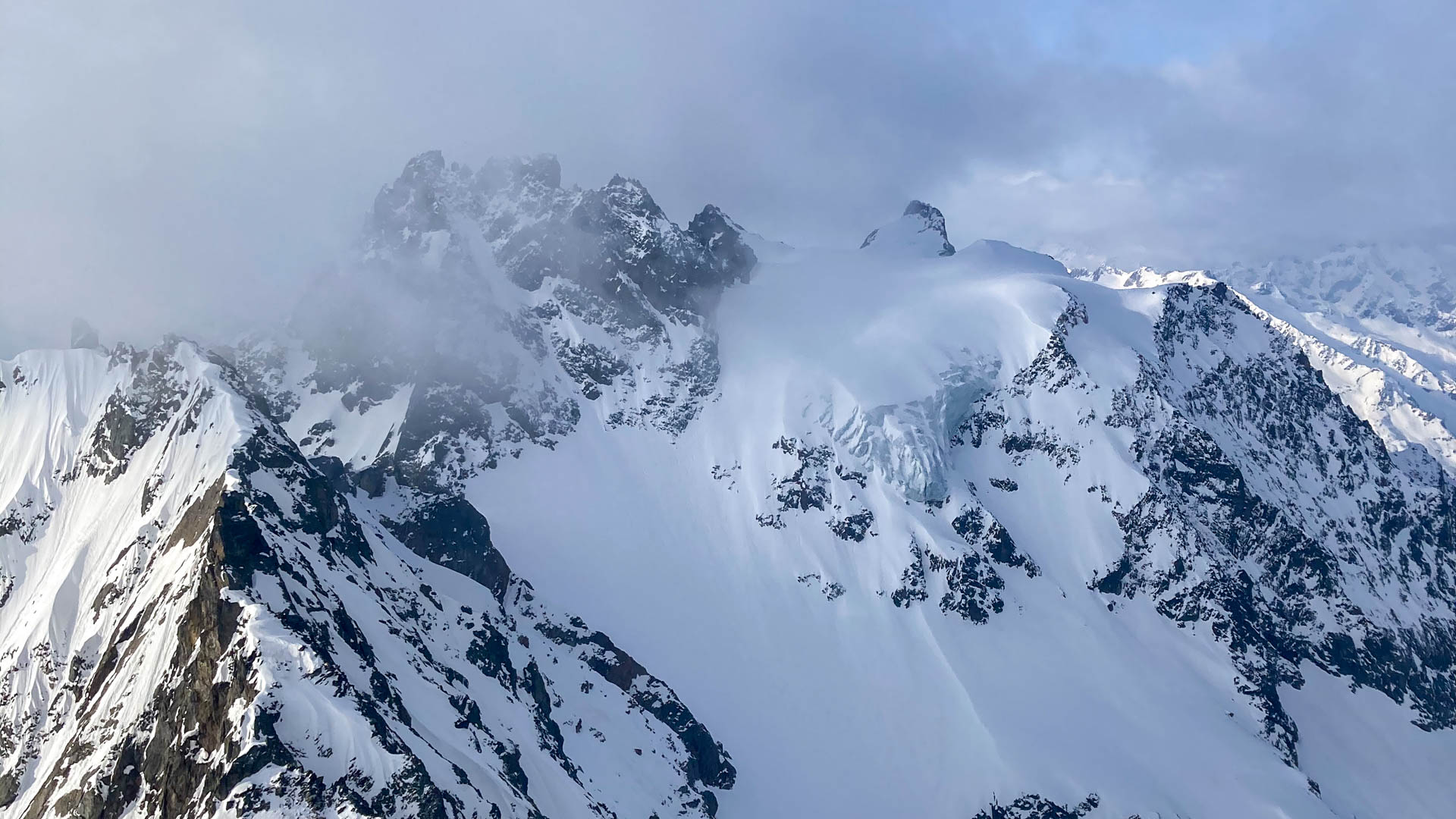 Skitour in den Urner Alpen: Gipfelpanorama mit Schneefeldern, vergletschertem Hochplateau und wolkenverhüllten Graten.