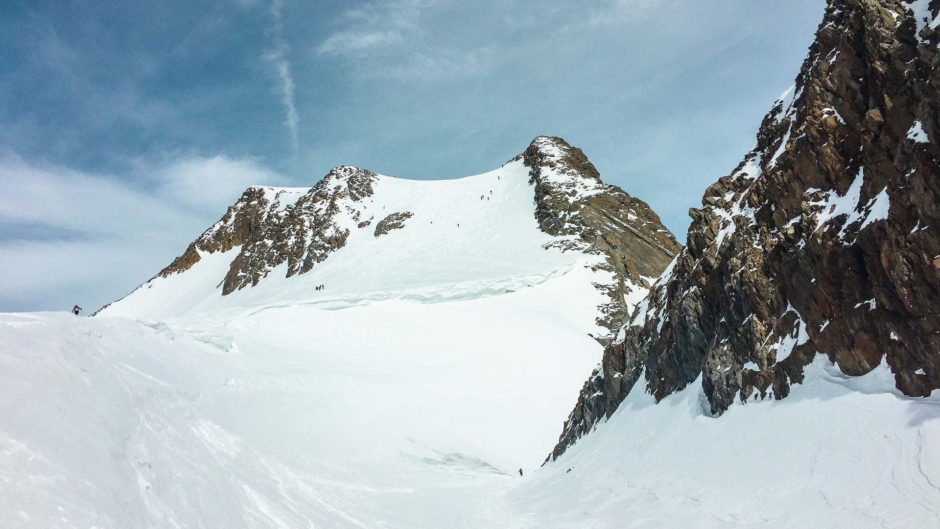 Mehrere Skitourengeher im Aufstieg über ein weitläufiges Firnfeld mit zwei felsigen Gipfeln im Ötztal.