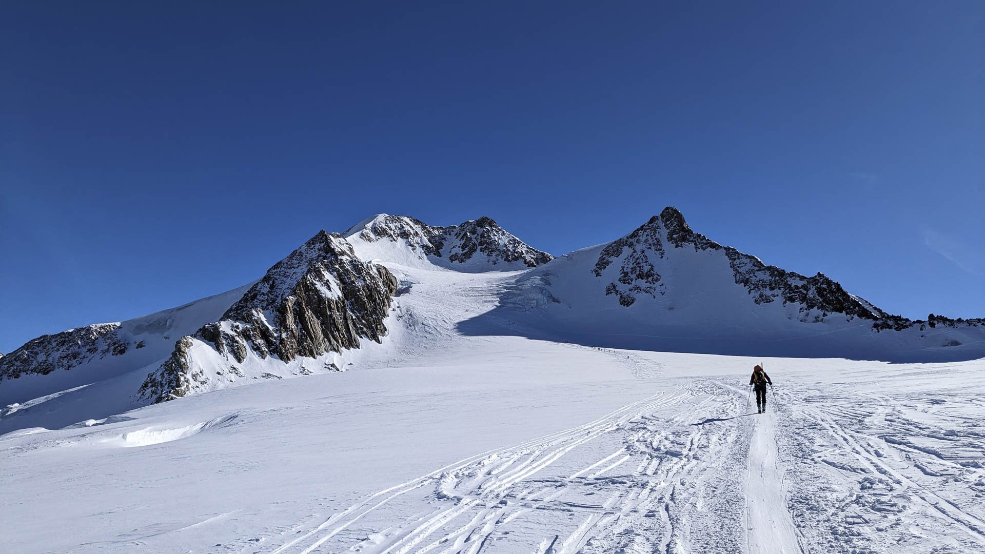 Skitourengeher steigt über ein weites Gletscherplateau in Tirol mit zwei verschneiten Gipfeln im Hintergrund.