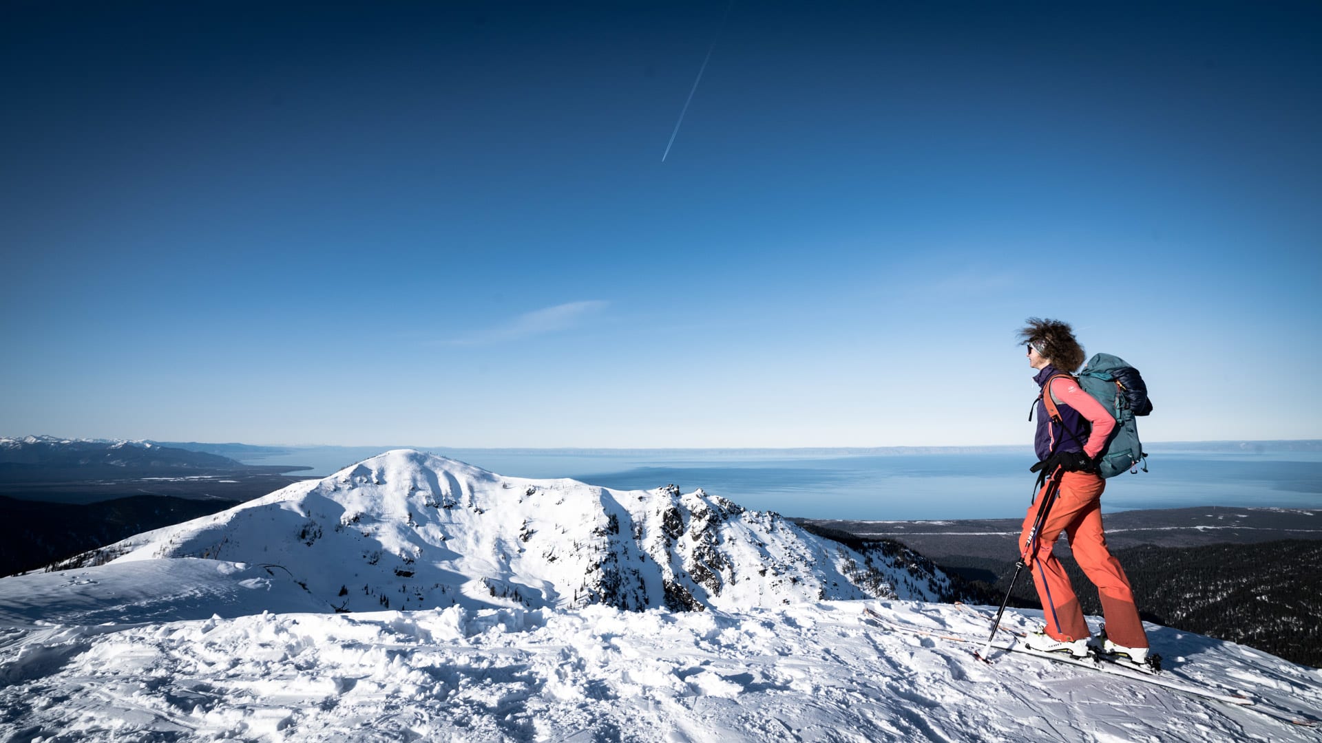 Skitourengeher steht auf schneebedecktem Berggrat mit Blick auf den Baikalsee und tiefblauen Winterhimmel.