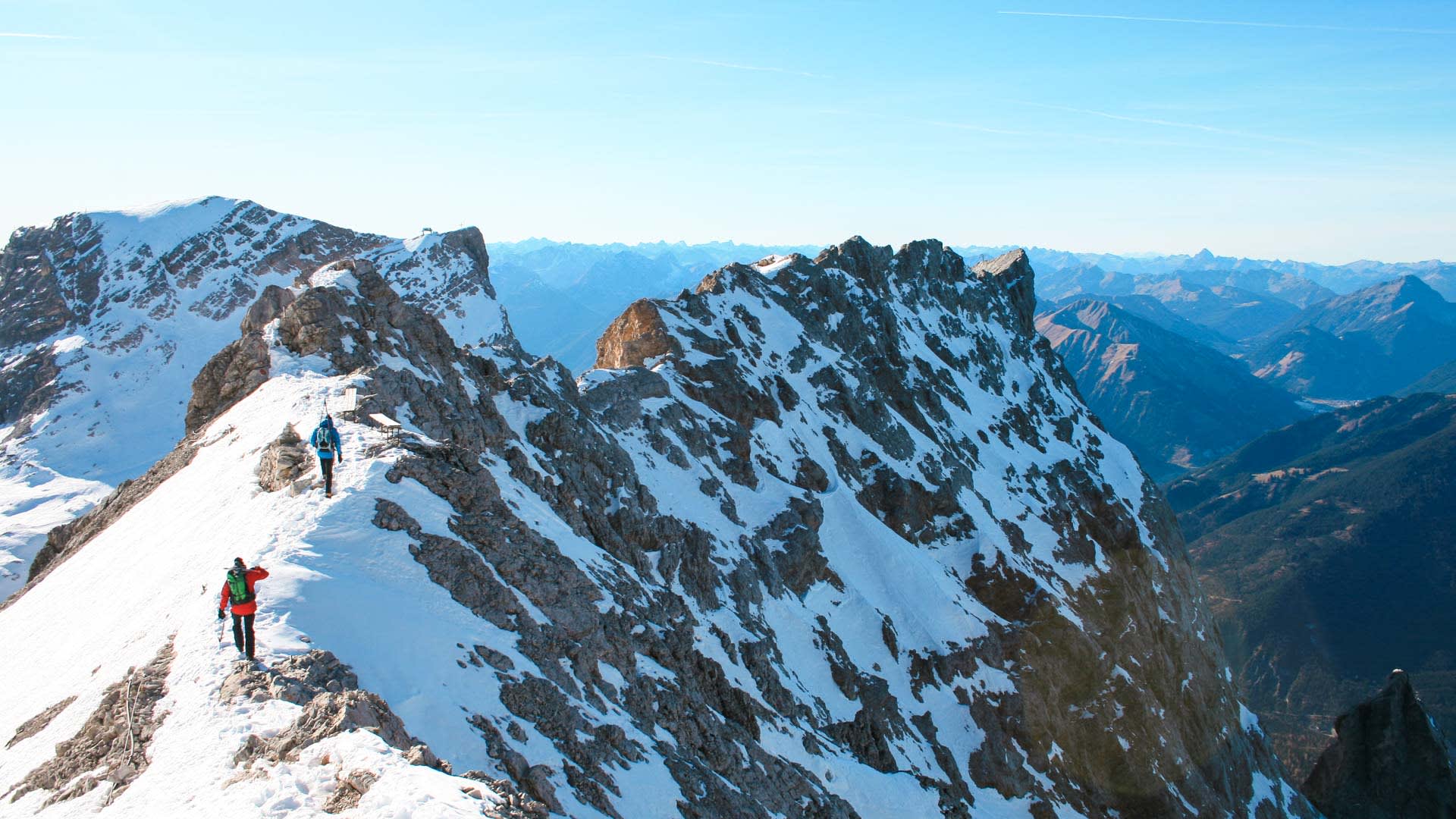 Zwei Freerider steigen auf einem schneebedeckten Felsengrat zur Neuen Welt bei Garmisch auf.