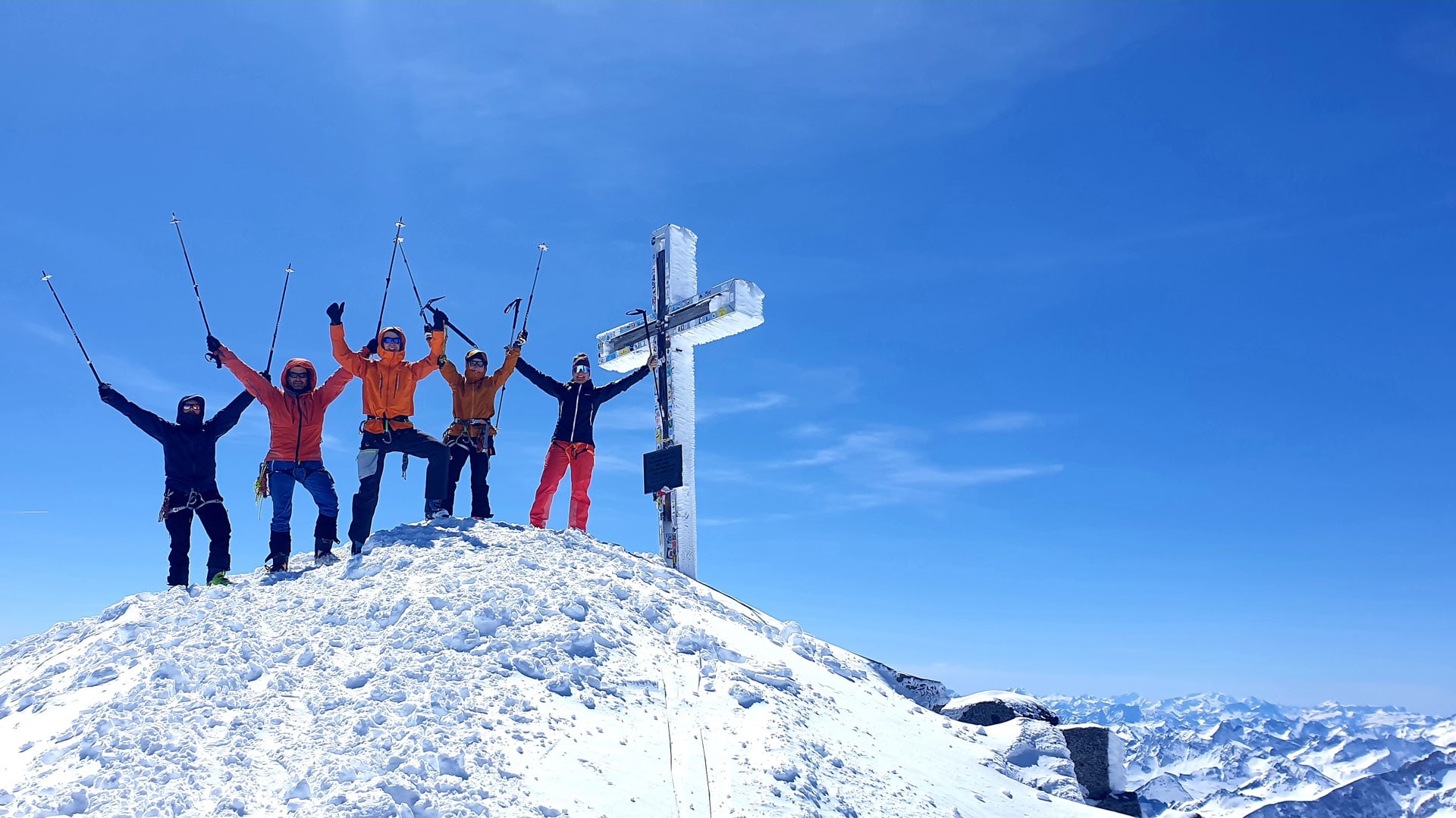 Fünf Skitourengeher feiern den Gipfelerfolg am vereisten Kreuz des Großvenedigers in den Hohen Tauern und heben Trekkingstöcke