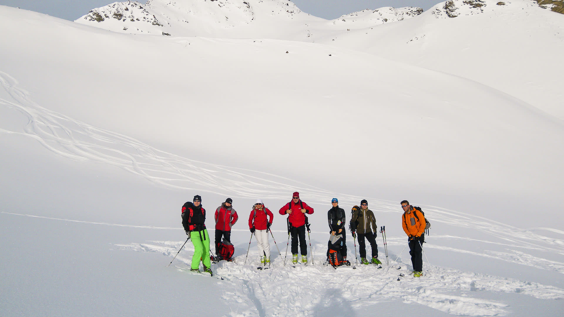Sieben Skitourengeher mit Skitouren-Ausrüstung stehen nebeneinander auf einem Schneehang bei der Heidelberger Hütte.