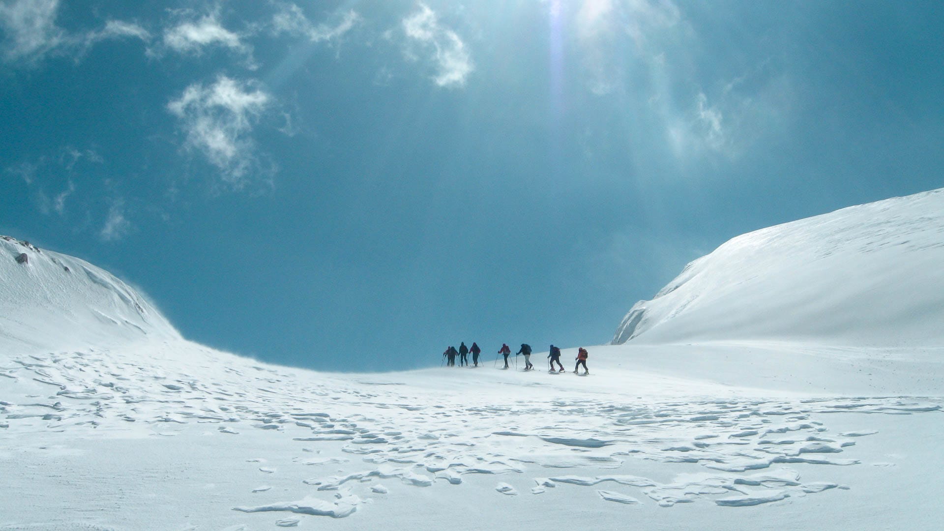 Gruppe von Skitourengehern steigt in Montenegro auf einem breiten Schneehang in Richtung Sattel auf, weite Hochgebirgslandschaft