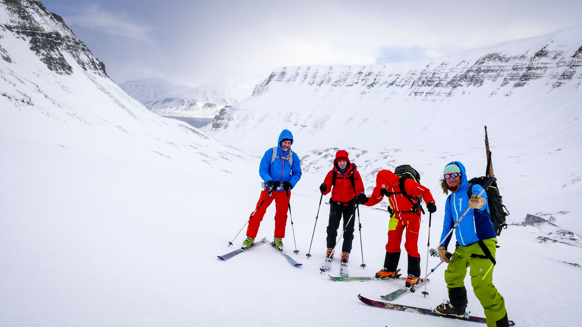 Vier Skitourengeher mit Rucksäcken pausieren im Trolldalen, Spitzbergen, vor felsigem Bergpanorama.