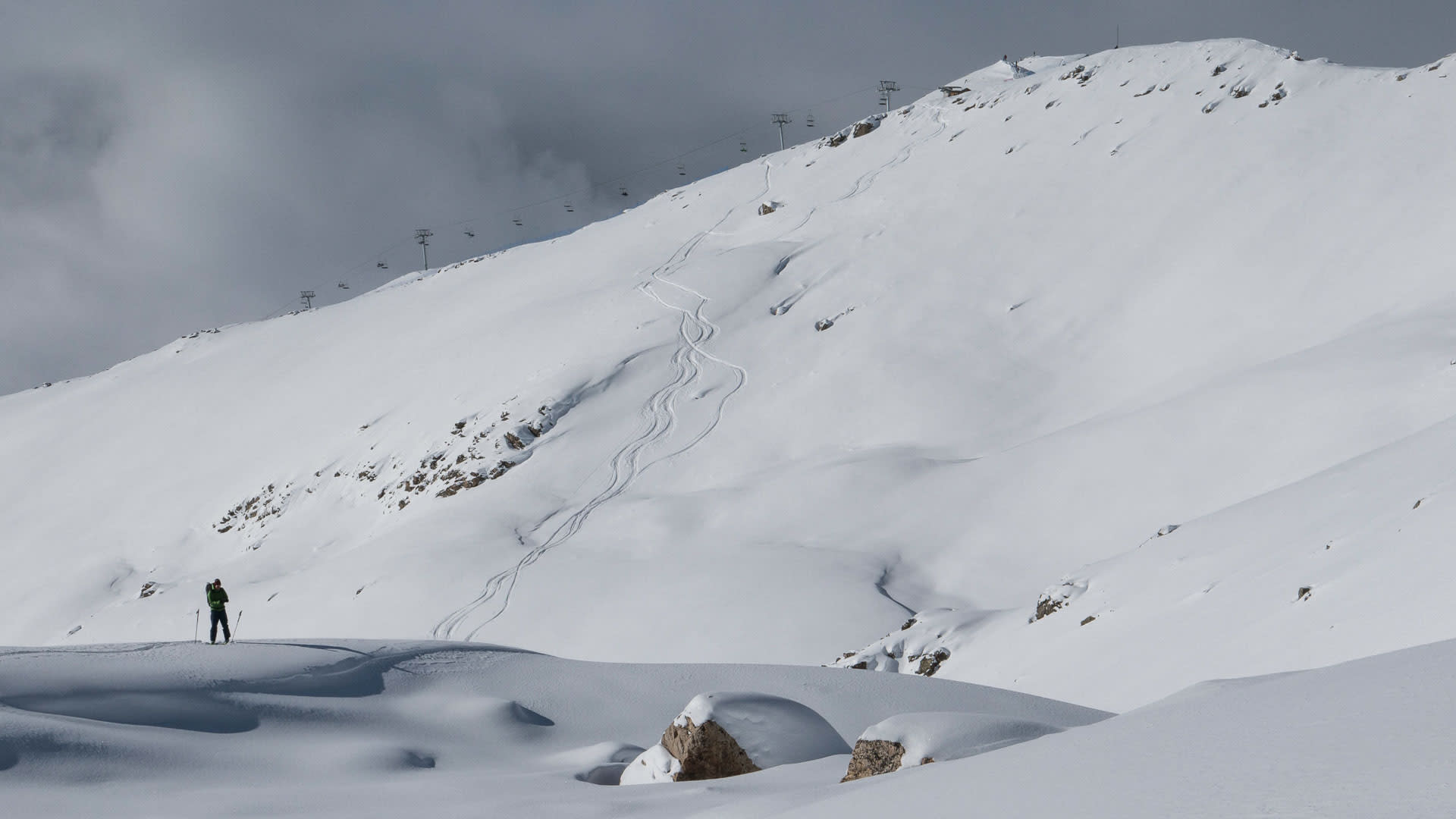 Skitourengeher pausiert auf tiefverschneitem Hang mit Seilbahnmasten im Skigebiet Swanetien, Georgien.