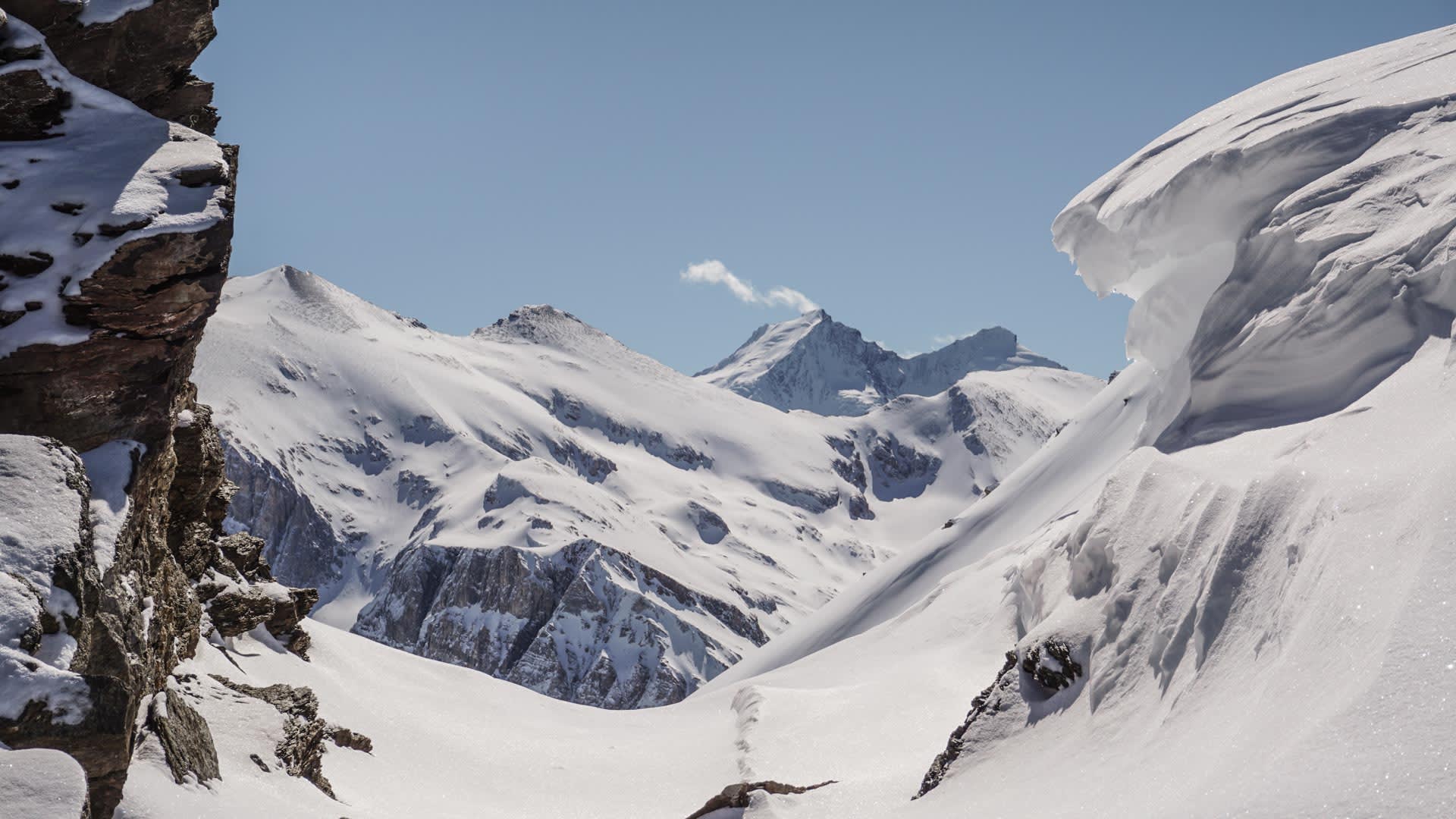 Skitour-Spur führt durch ein weites, schneebedecktes Hochtal in der Schweiz mit vergletscherten Gipfeln im Hintergrund.