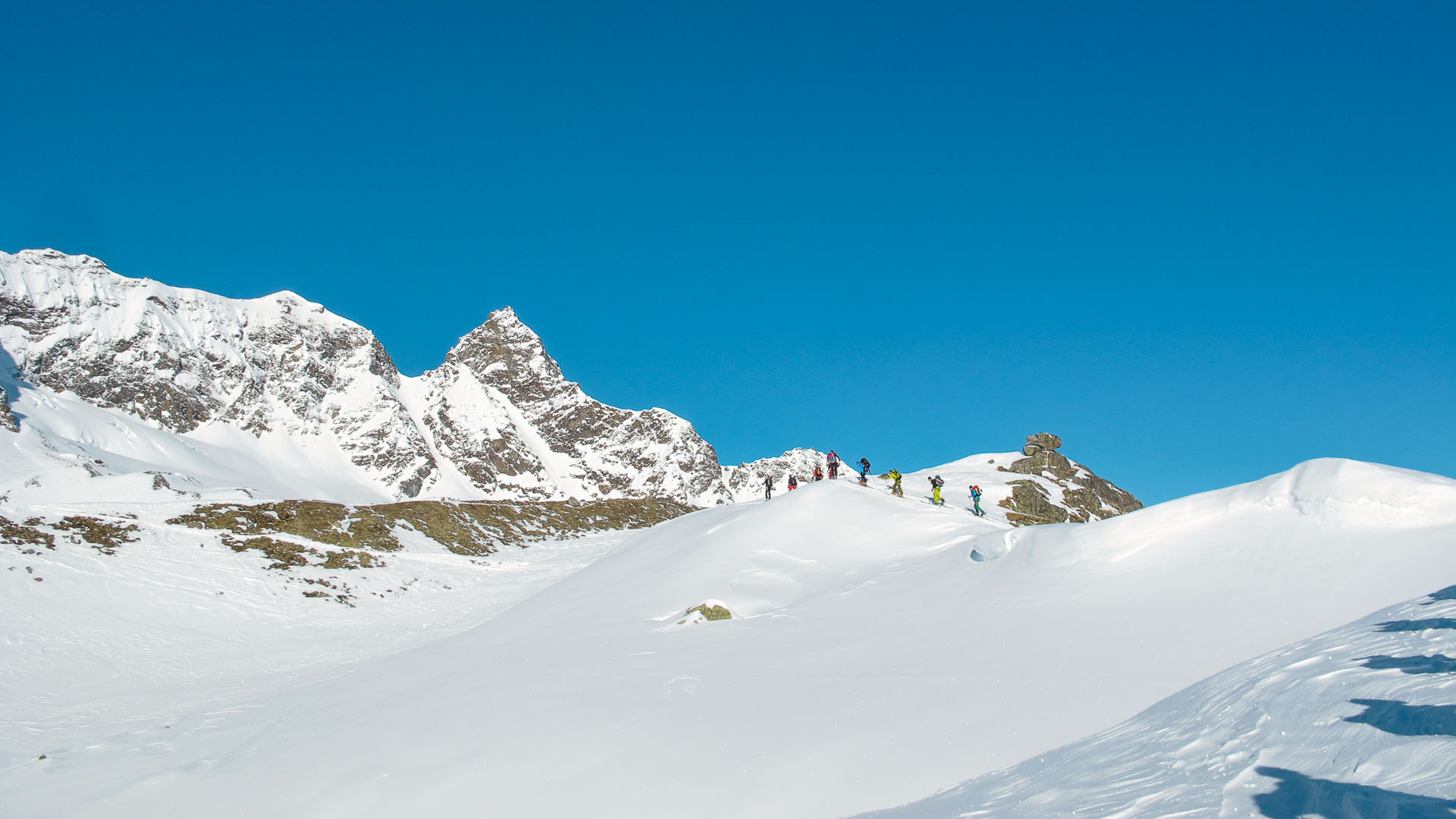 Gruppe von sieben bis acht Skitourengehern auf der Kammlinie beim Aufstieg zum Piz Buin im Winter.