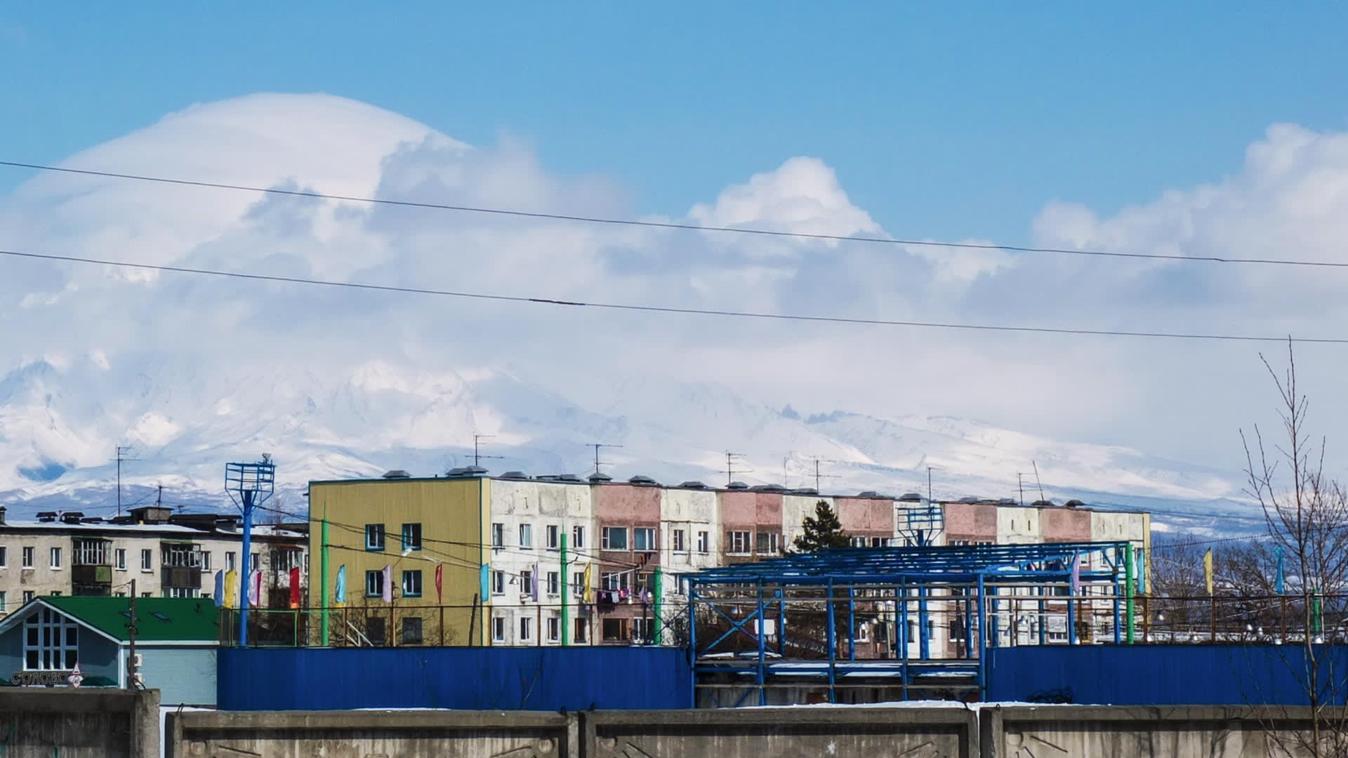 Skitour Kamtschatka – Stadtansicht Petropavlovsk mit mehrstöckigen Wohnhäusern und schneebedeckter Vulkankette im Hintergrund