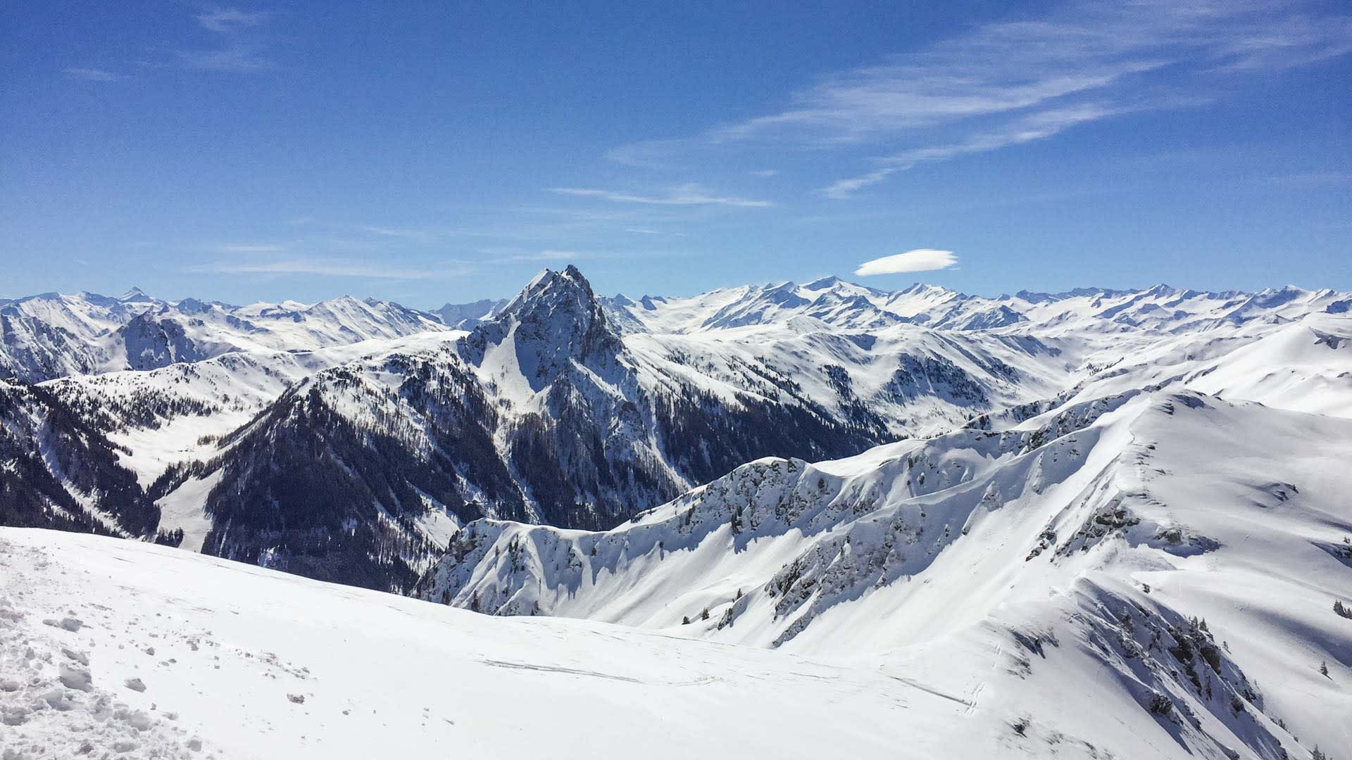 Skitour rund um Kitzbühel: Weitwinkelpanorama von einem verschneiten Grat auf Bergkämme und einen markanten Felsgipfel