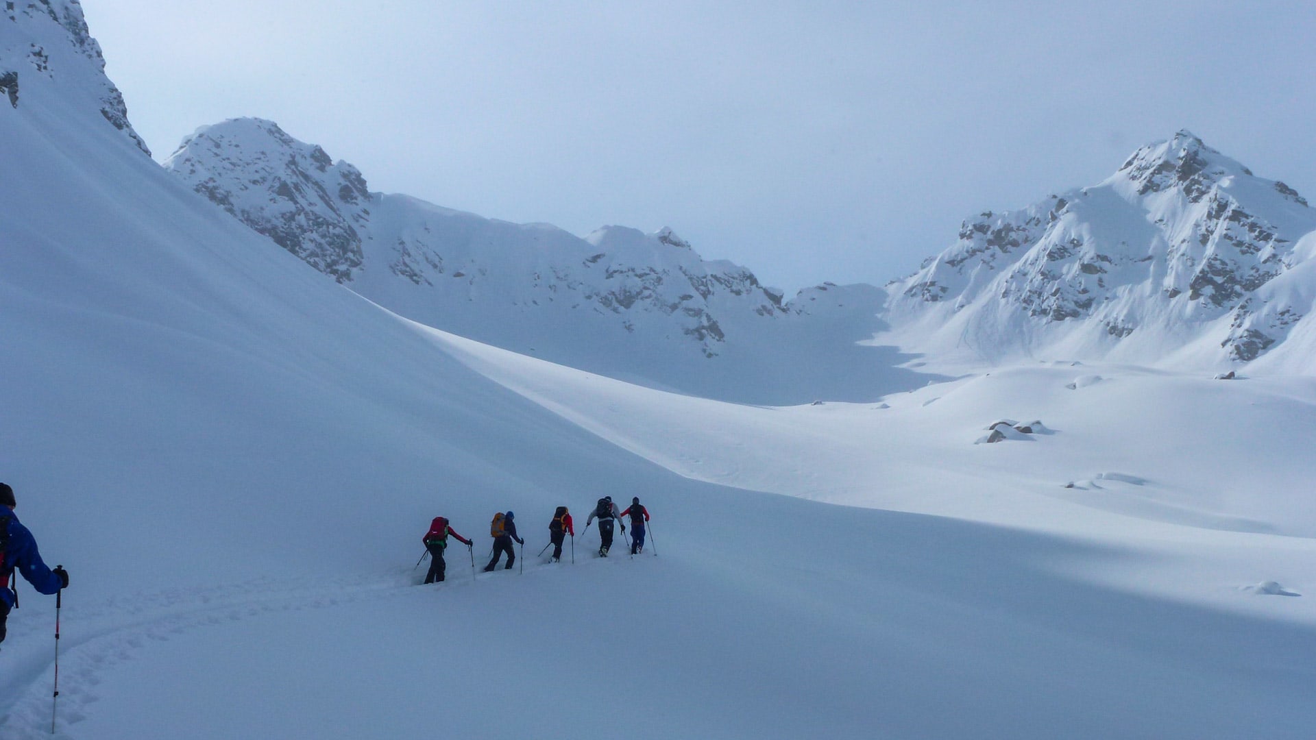 Skitour Silvretta: Sechs Skitourengeher mit Fellen steigen in Reihe durch den schneebedeckten Talkessel zur Kromerlücke auf.