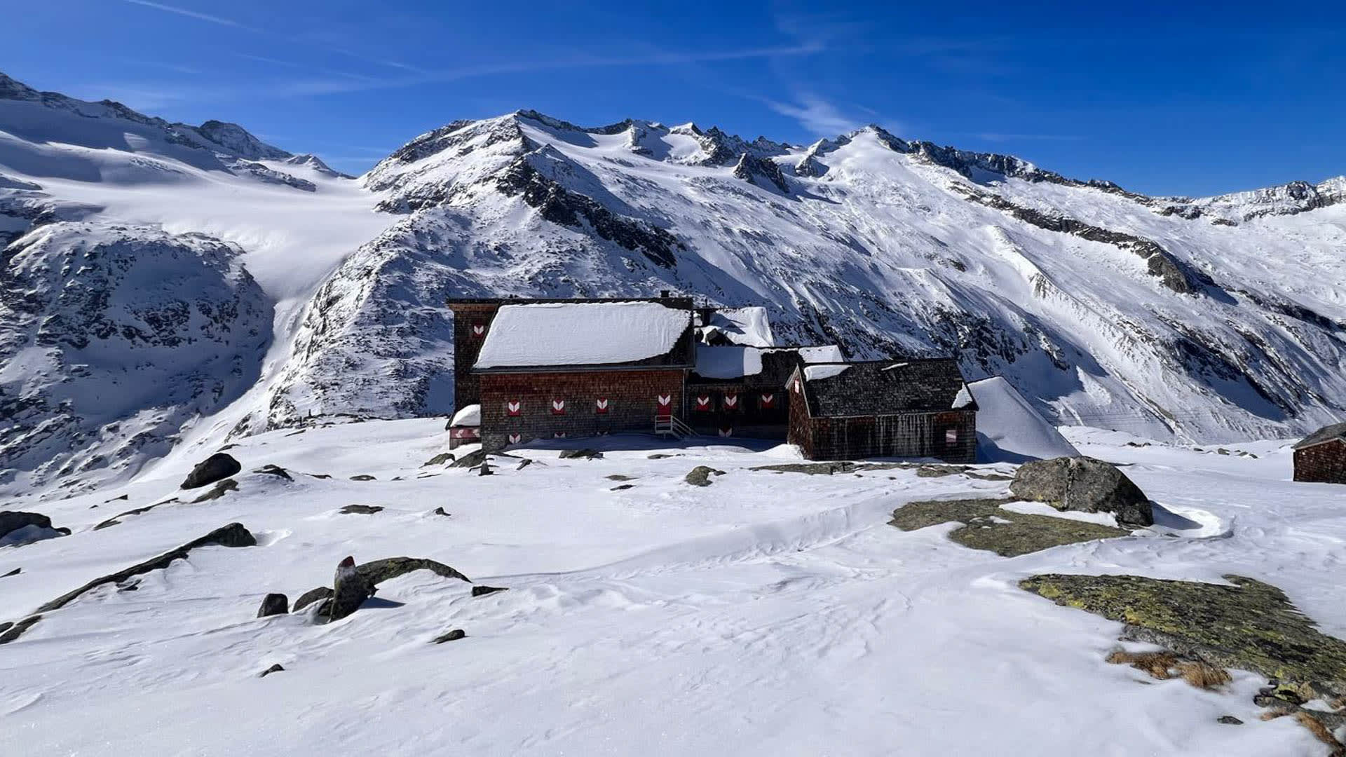 Skitour Hohe Tauern: Kürsinger Hütte auf verschneitem Plateau vor vergletschertem Bergmassiv mit Felsgraten