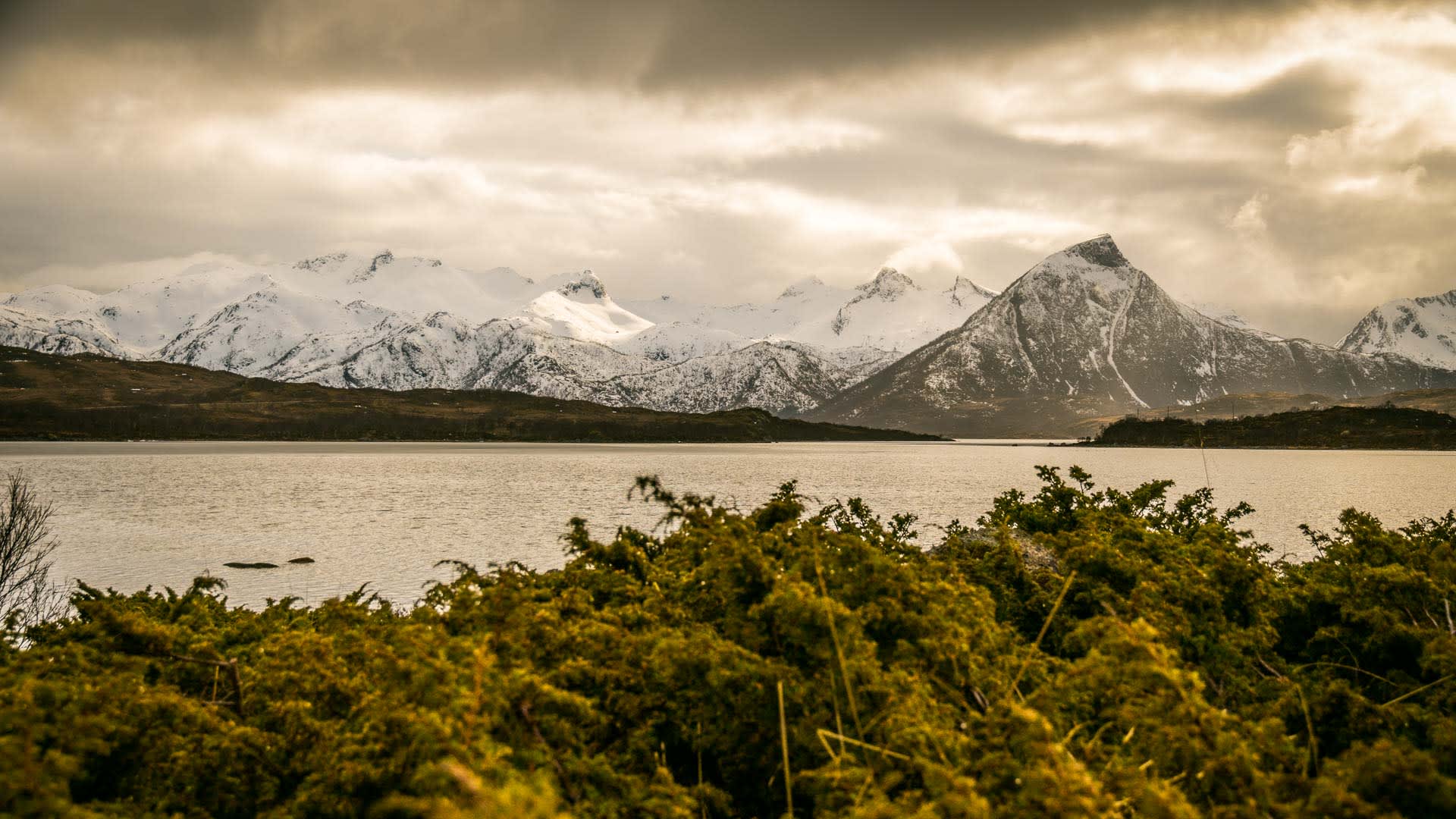 Skitour auf den Lofoten: Ruhige Fjordbucht mit weitläufiger schneebedeckter Gebirgskette und markant spitzem Gipfel im Hintergrund