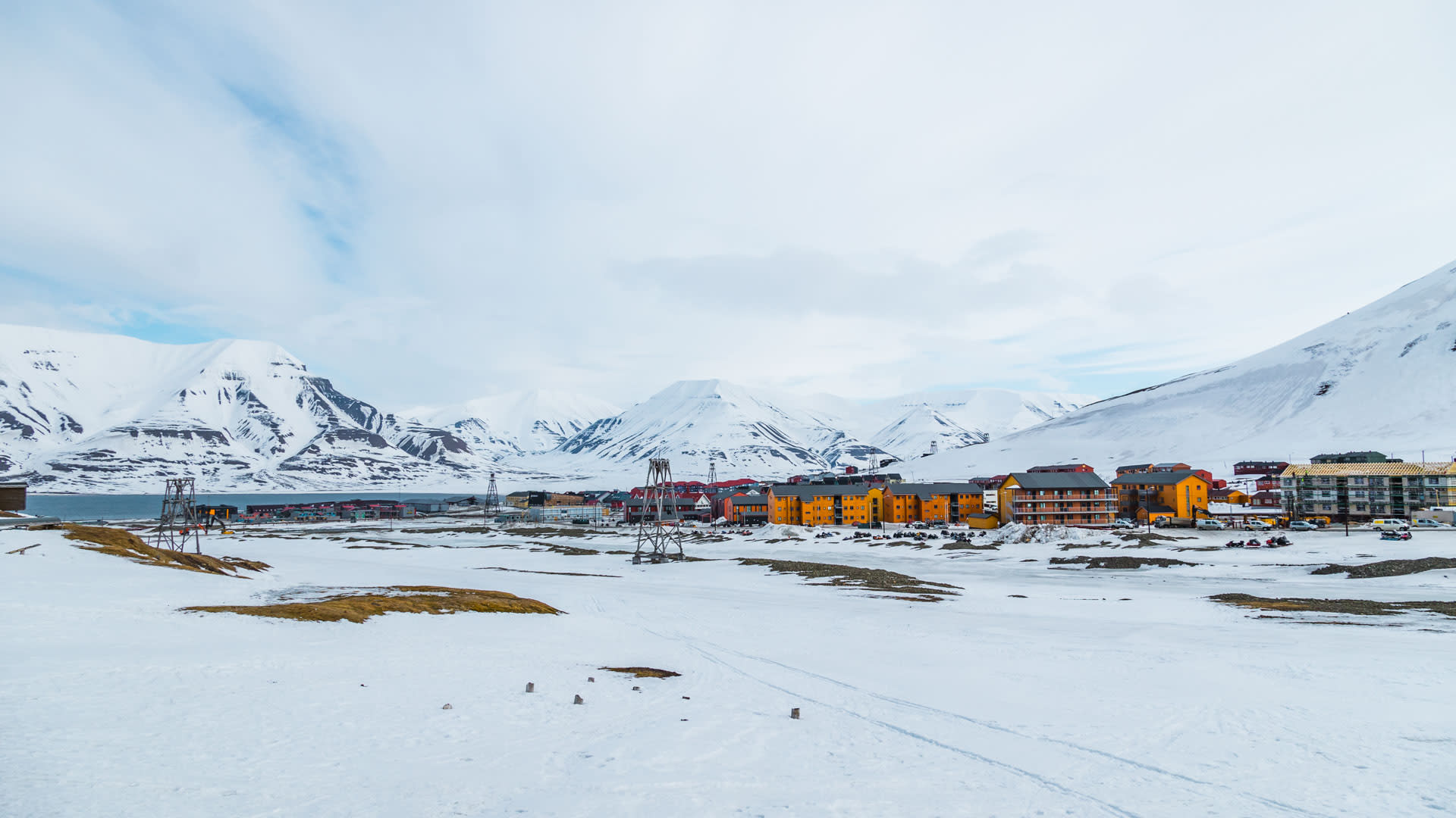 Blick auf die farbigen Gebäude von Longyearbyen in Spitzbergen, umgeben von schneebedeckten Bergen und einem Fjord.