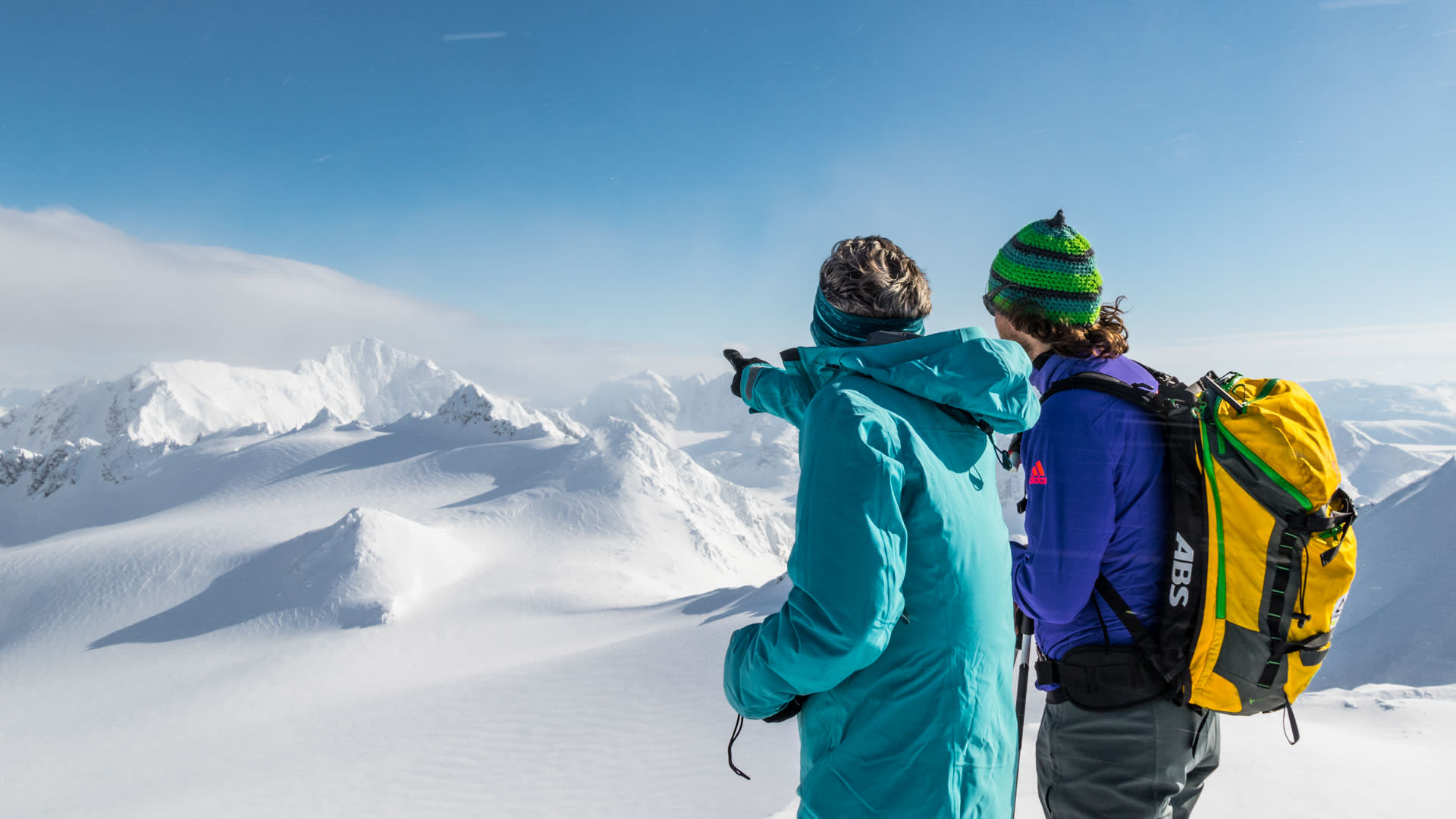Zwei Personen auf einer Skitour am Lyngen Fjord blicken auf das weitläufige verschneite Bergpanorama der Lyngen Alps