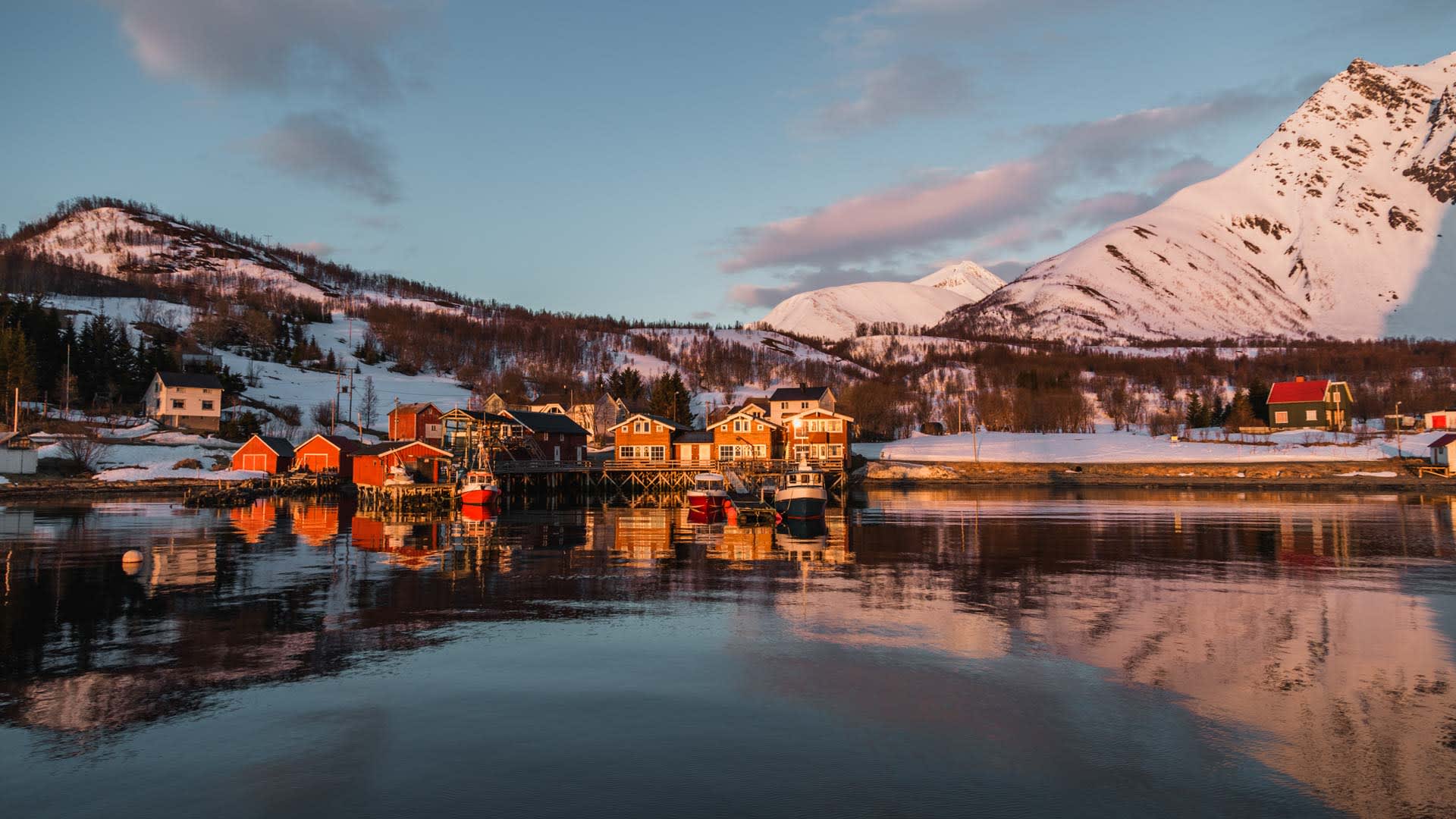 Skitouren Lyngenalpen: Fjordsiedlung mit roten Bootshäusern und schneebedeckten Bergen im Abendlicht der Mitternachtssonne.