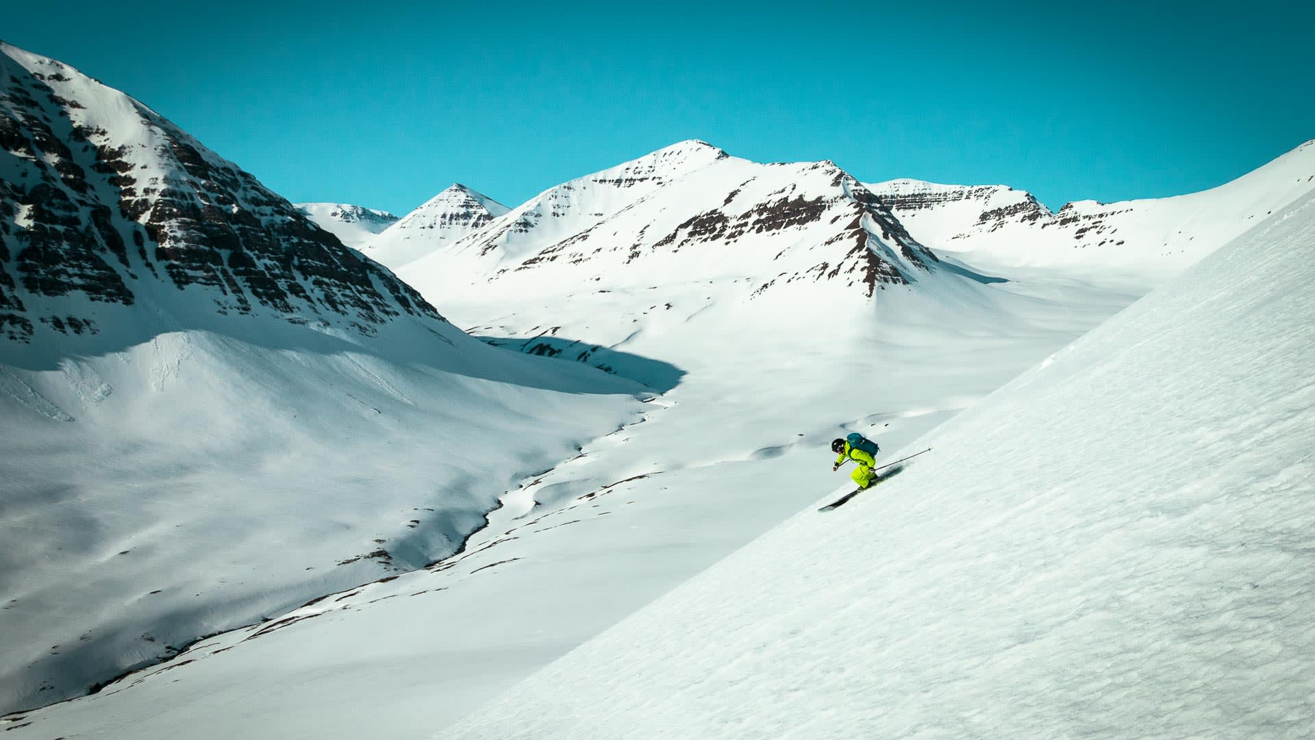 Skitourengeher fährt unverspurten Steilhang in einem weiten Hochtal auf Island im Winterlicht ab.