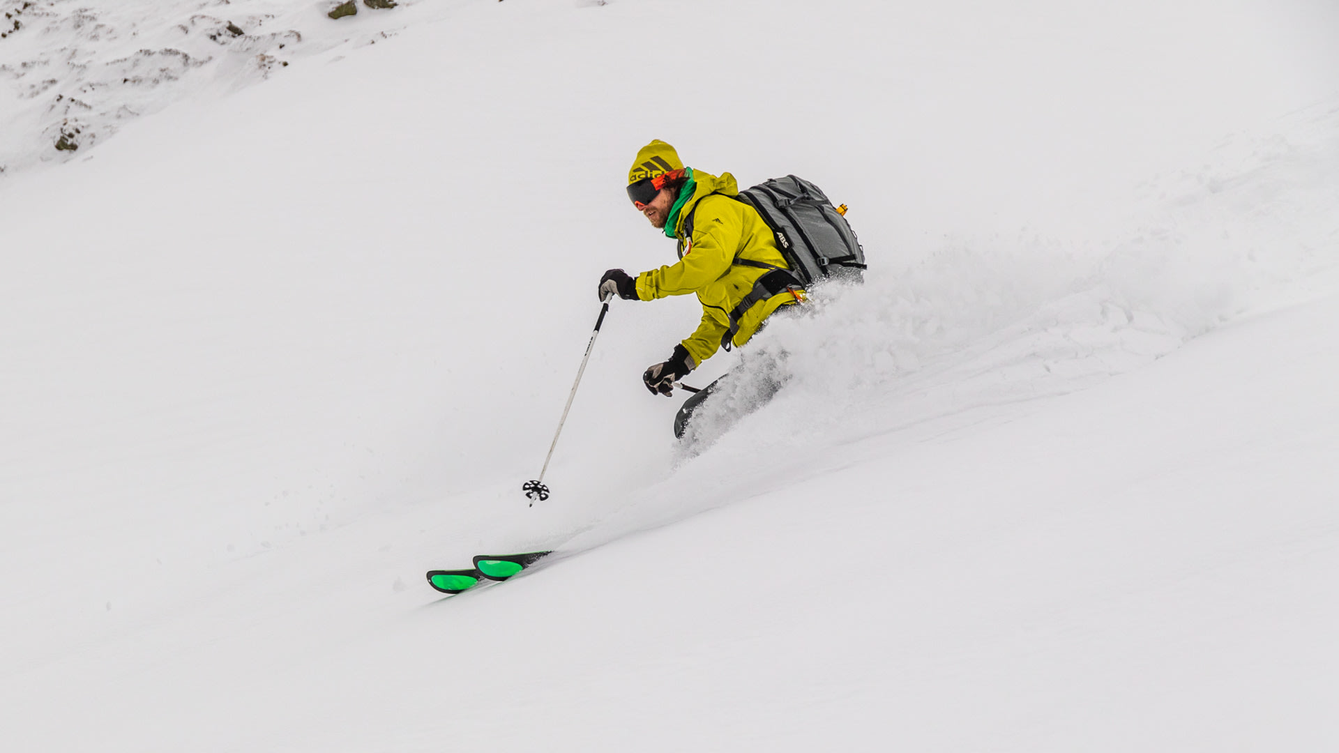 Person auf Skitour in den rumänischen Karpaten fährt in einer Kurve durch tiefen Pulverschnee mit aufgewirbelter Schneewolke.