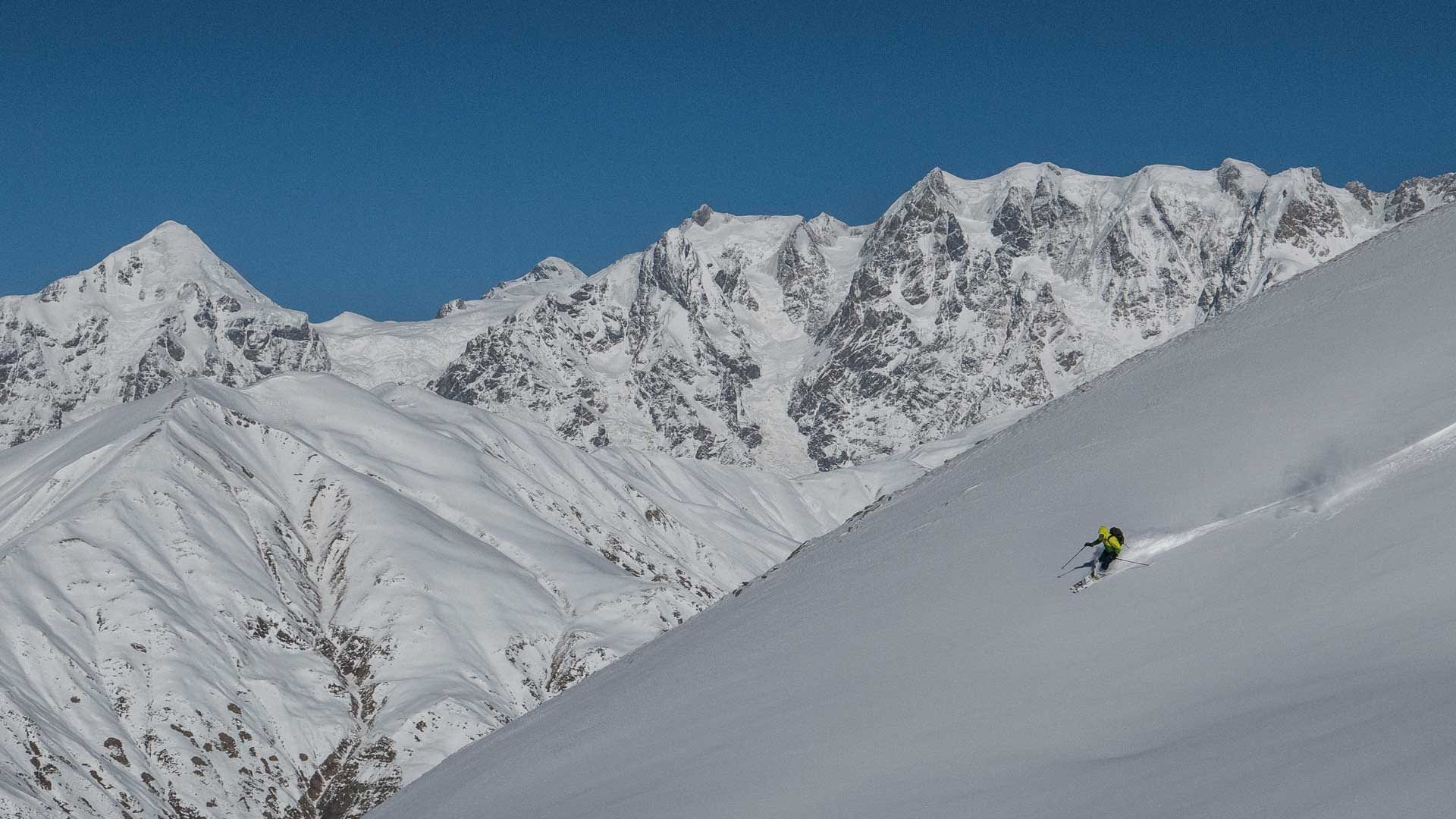 Skitourengeher fährt einen unverspurten Pulverschneehang in Swanetien ab, im Hintergrund vergletscherte Gipfel.