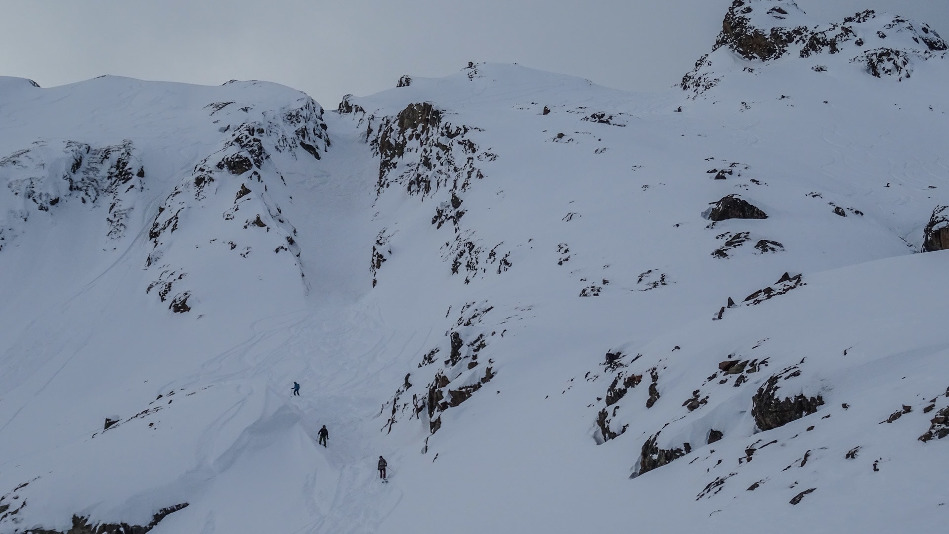 Drei Freerider steigen in einer Linie durch eine verschneite Bergrinne im Stubai auf, Felsformationen sichtbar.