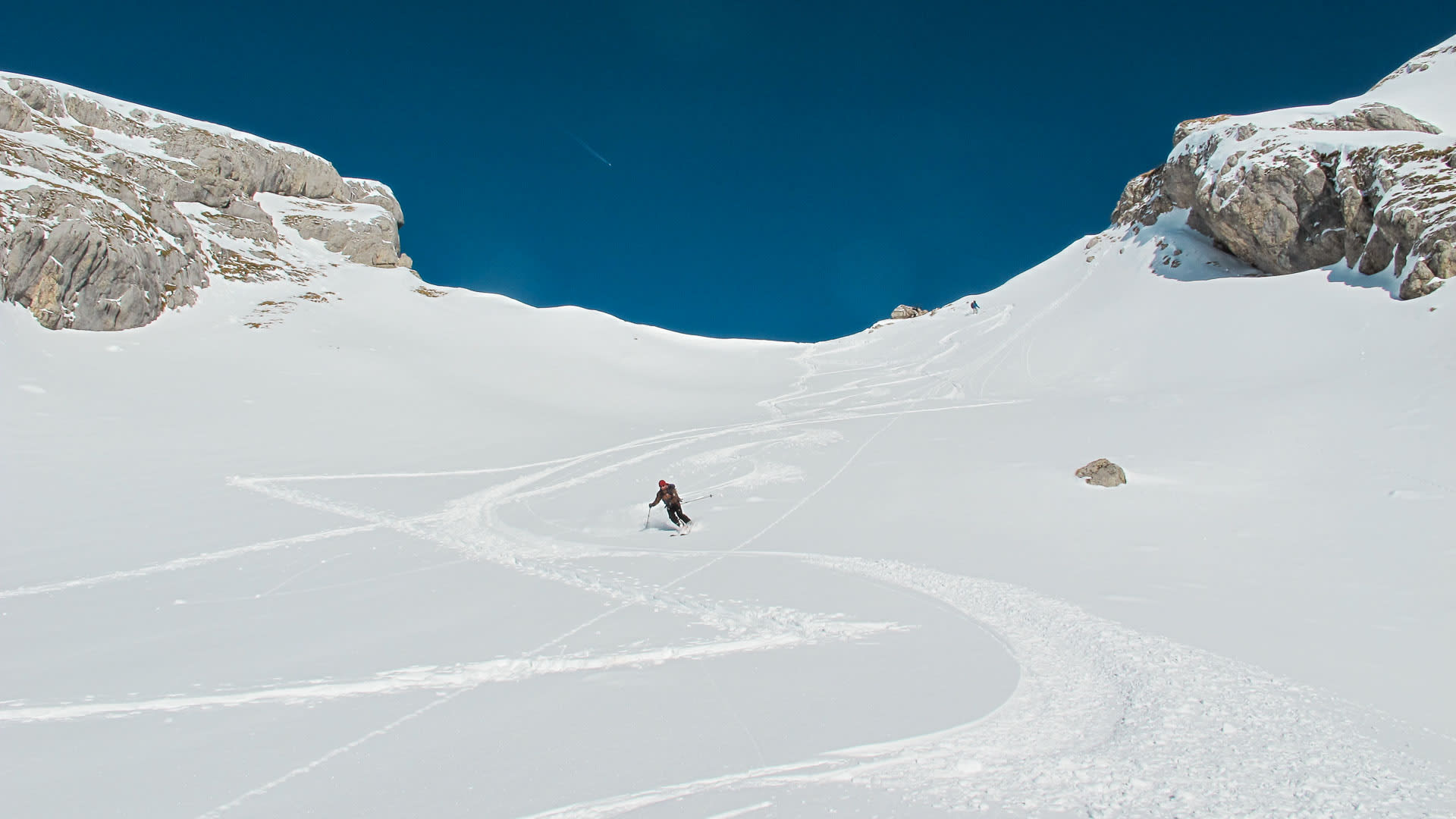 Skitour im Rofan: Person mit rotem Helm fährt auf verschneitem Steilhang ab, flankiert von hellen Kalksteinwänden