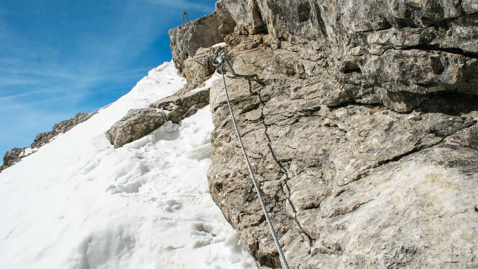 Skitour Neue Welt: Klettersteig-Drahtseil an Kalkfels neben steiler Schneerinne mit Trittstufenspuren im Winter.