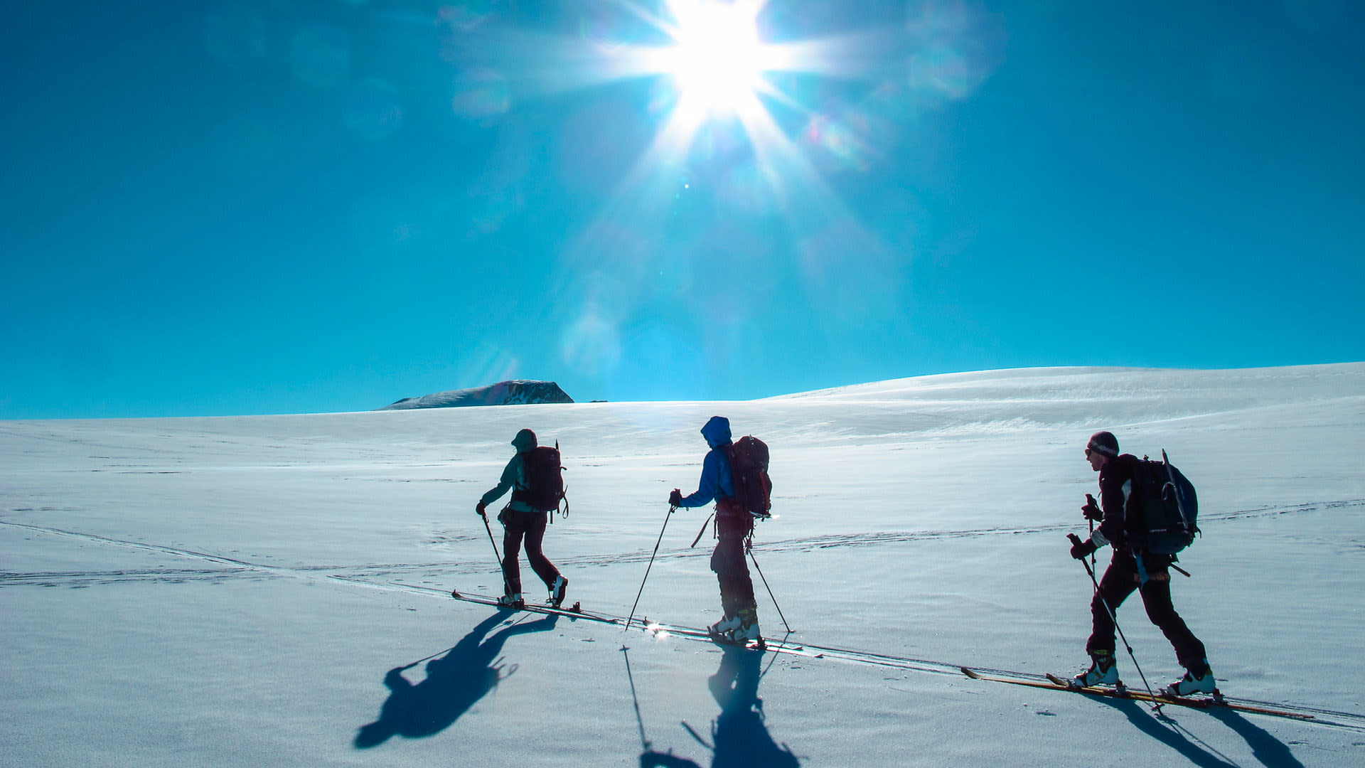 Drei Skitourengeher als Silhouetten mit Ski und Fellen im Gegenlicht der tief stehenden Sonne beim Aufstieg im Wallis.