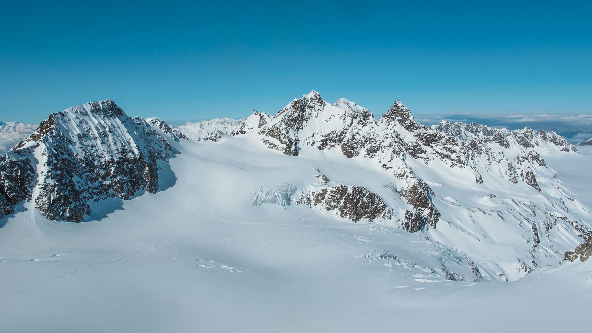Skitour Silvrettahorn: Blick vom Piz Buin über den Silvretta-Gletscher mit Gletscherspalten und Bergkette im Hintergrund.