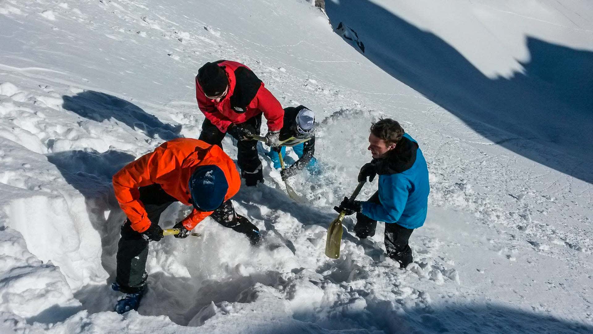 Vier Skitourengeher schaufeln mit Lawinenschaufeln eine Grube im Schneehang beim Skitourenkurs im Rofangebirge.