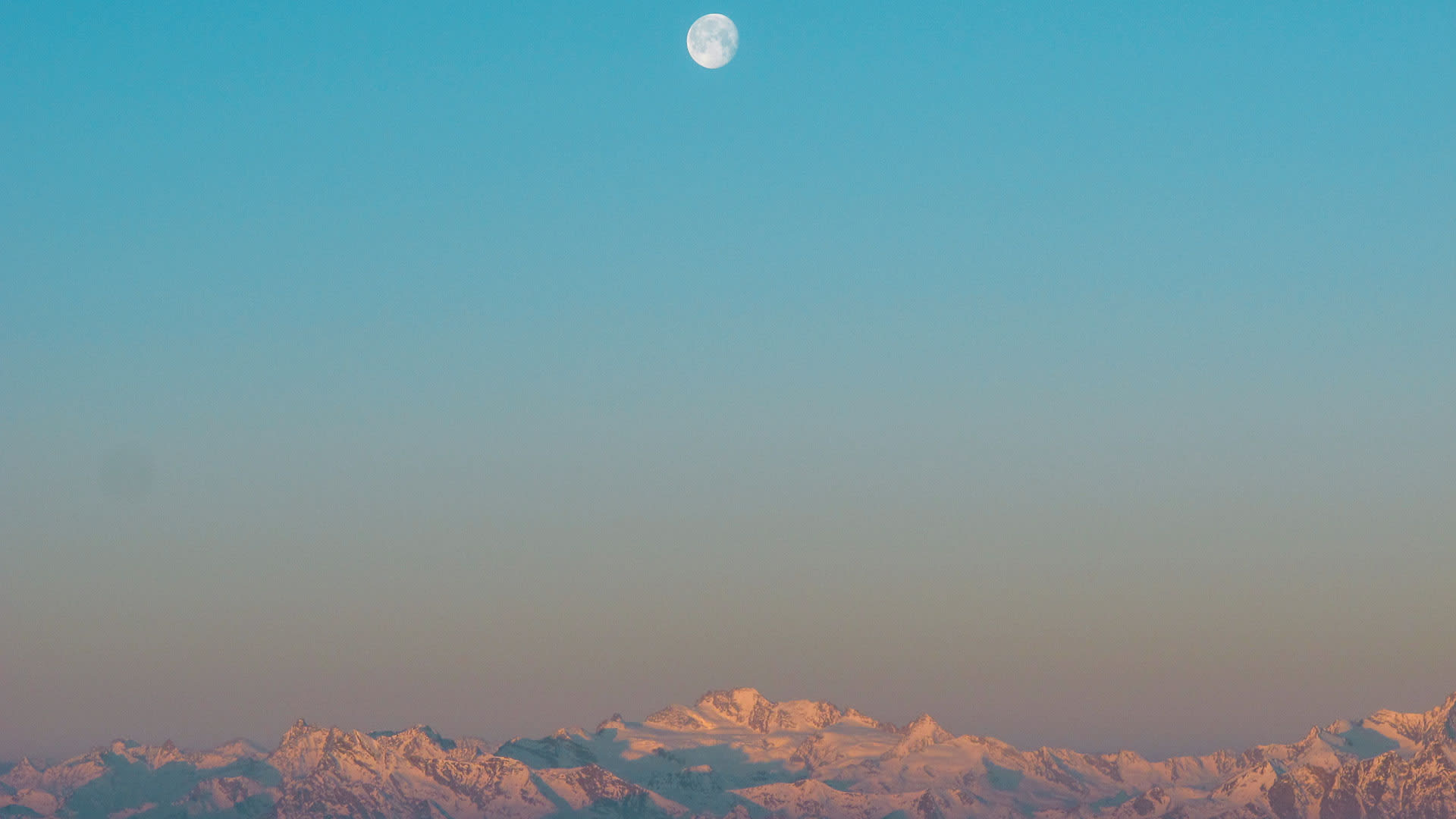 Skitour-Panorama bei der Mantova Hütte im Wallis: verschneite Bergkette im Morgenrot mit sichtbarem Mond am türkisblauen Himmel.