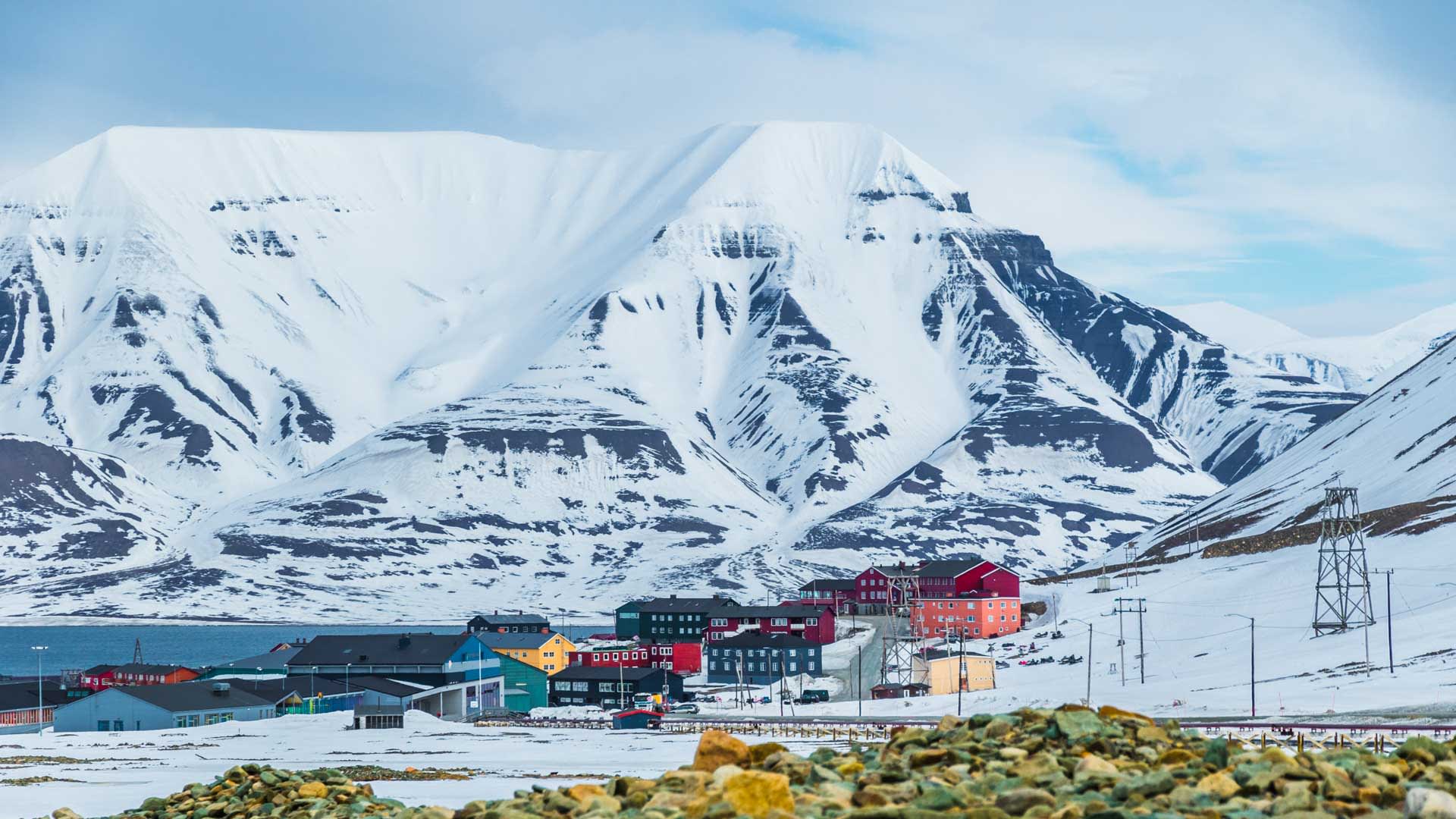 Skitour Spitzbergen: Arktische Siedlung in kräftigen Farben vor schneebedeckten Tafelbergen mit steilen Felswänden