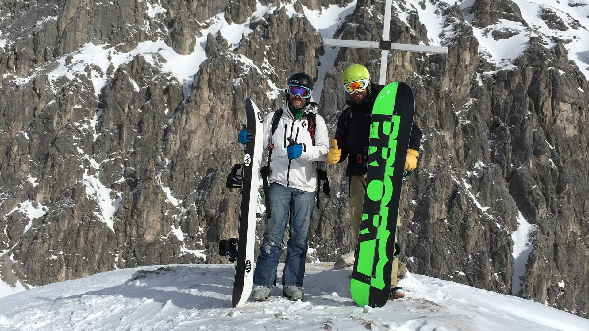 Zwei Freerider mit Snowboards am Gipfelkreuz bei Garmisch-Partenkirchen, Daumen nach oben.