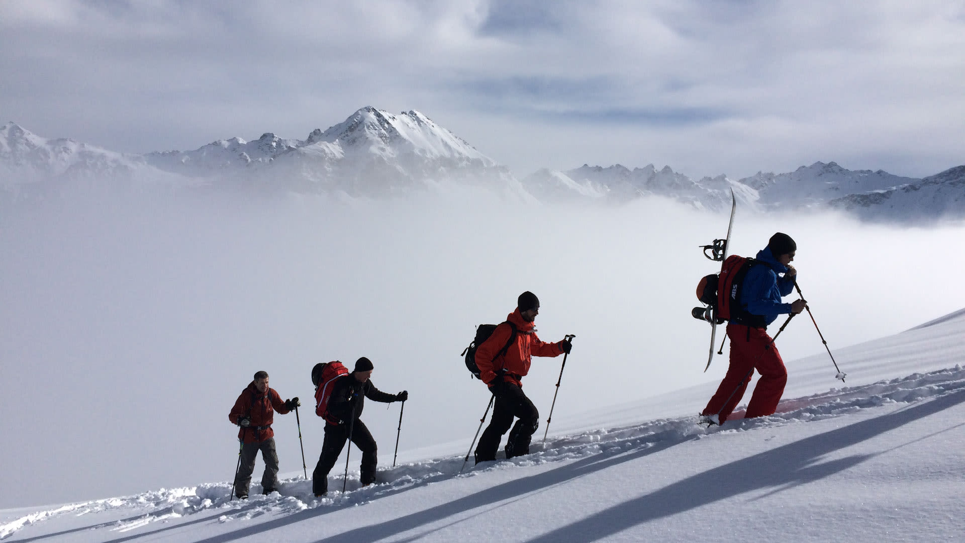 Vier Freerider steigen mit Splitboard und Skitouren-Fellen in der Silvretta durch eine Aufstiegsspur im Schnee auf.
