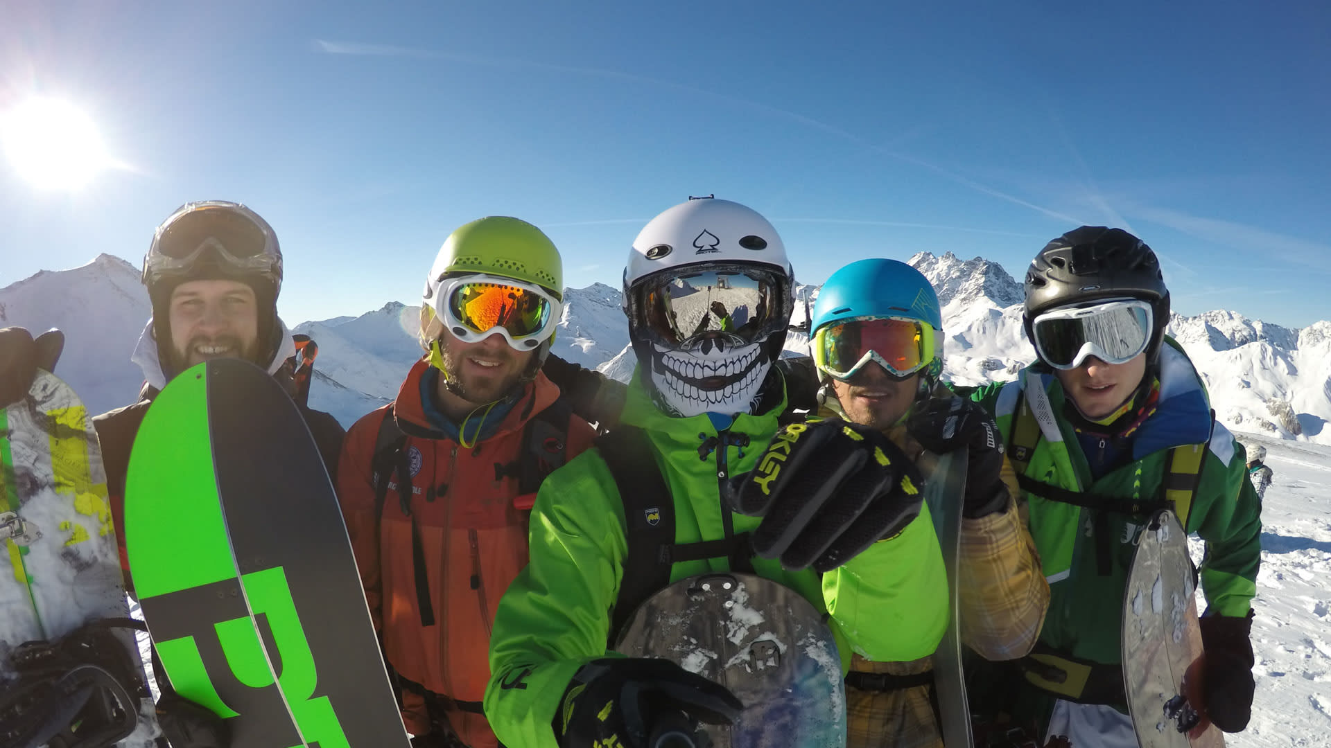 Fünf Freerider mit Helmen und Snowboards beim Splitboardkurs in den Tuxer Alpen vor verschneiten Gipfeln.